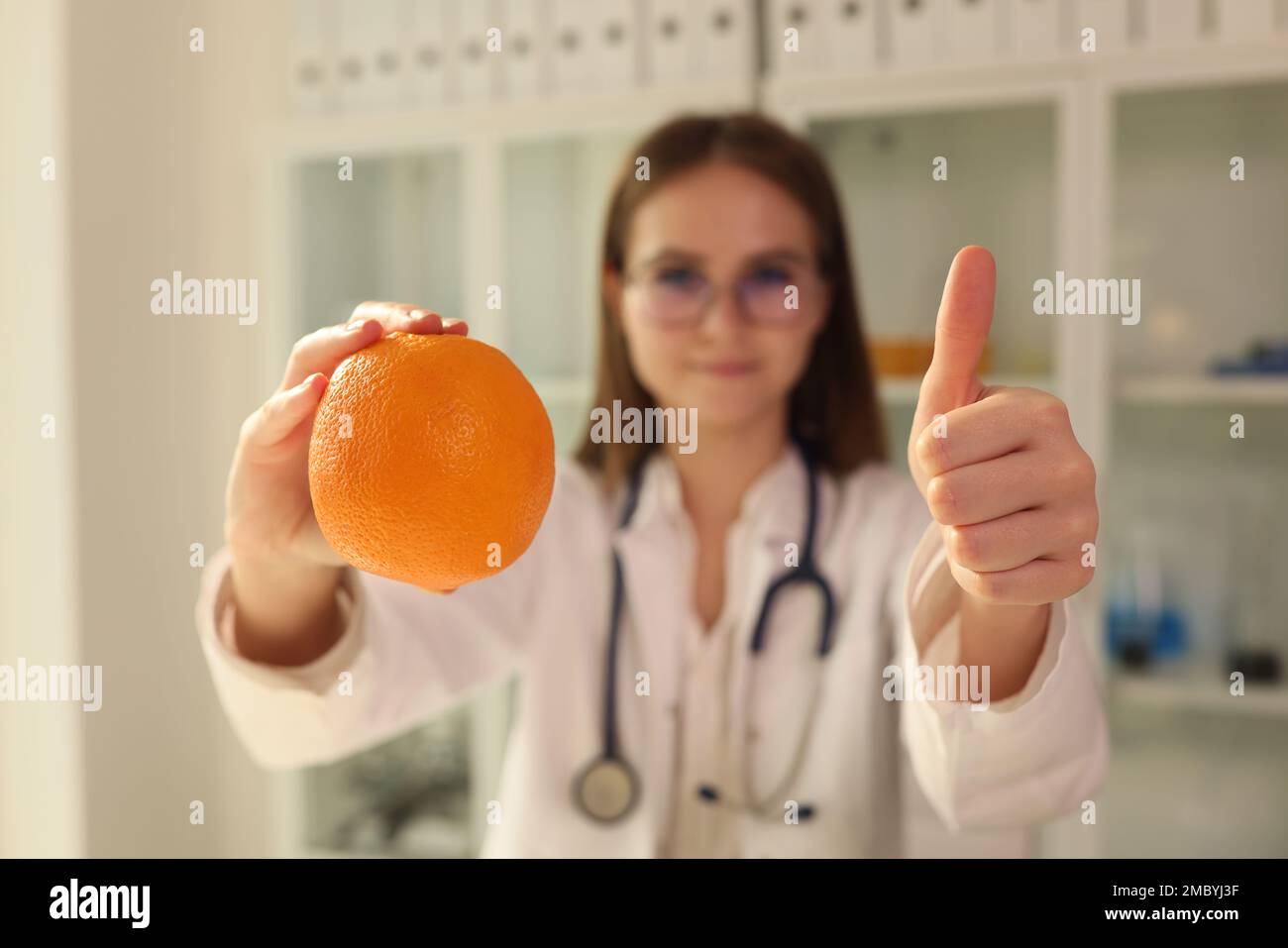 Medico nutrizionista tenendo arancione nelle sue mani e mostrando pollici su primo piano Foto Stock