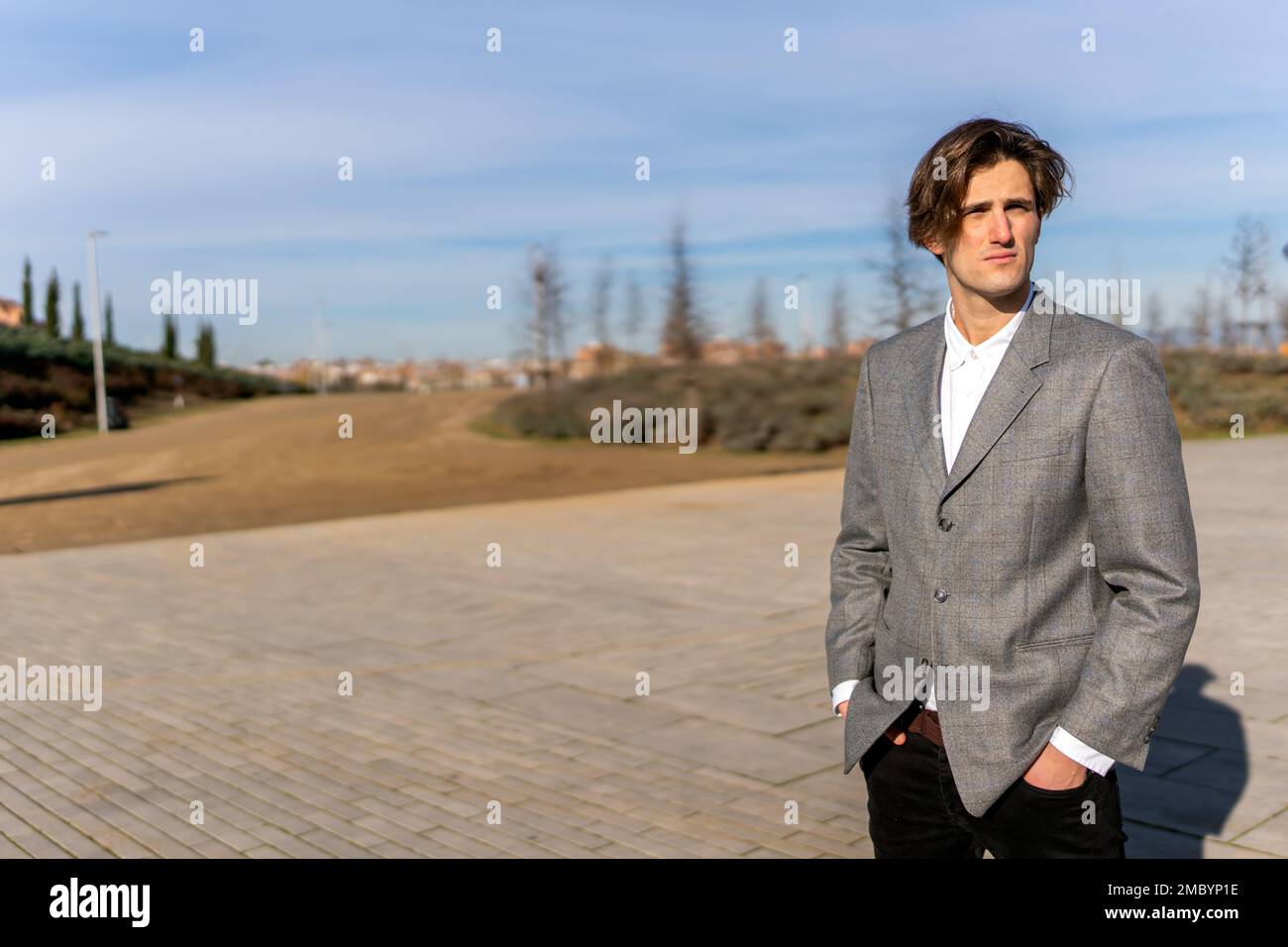 Giovane uomo d'affari premuroso in abiti formali in piedi sul passaggio pavimentato con le mani in tasca e guardando lontano Foto Stock