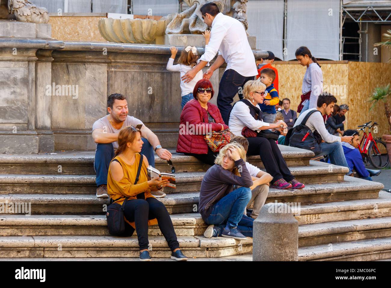 Un gruppo di persone che riposano sui gradini della Fontana di Santa Maria in Trastevere a Roma. Foto Stock