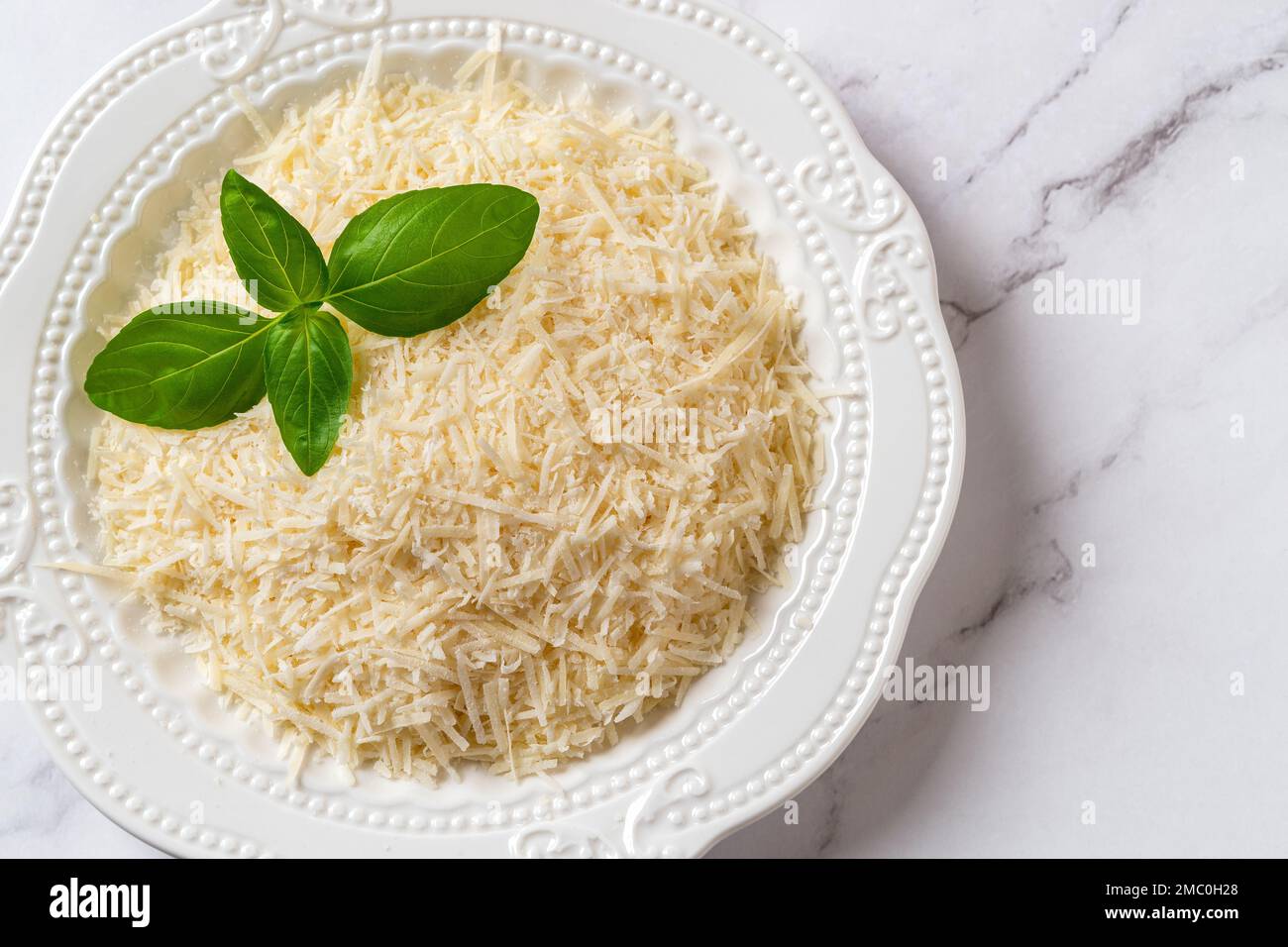 Parmigiano grattugiato su un primo piano. Piatto di grana padano grattugiato su fondo marmoreo. Formaggio italiano duro preparato per la cottura. Vista dall'alto. Foto Stock