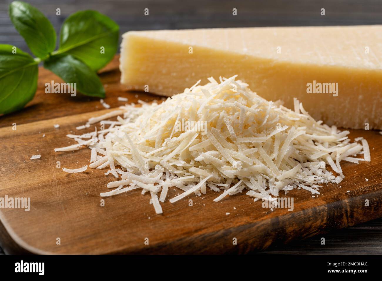 Cumulo di grana padano grattugiato primo piano. Gustoso parmigiano grattugiato e zeppa intera su tagliere di legno. Delizioso prodotto lattiero-caseario. Formaggio italiano. Foto Stock