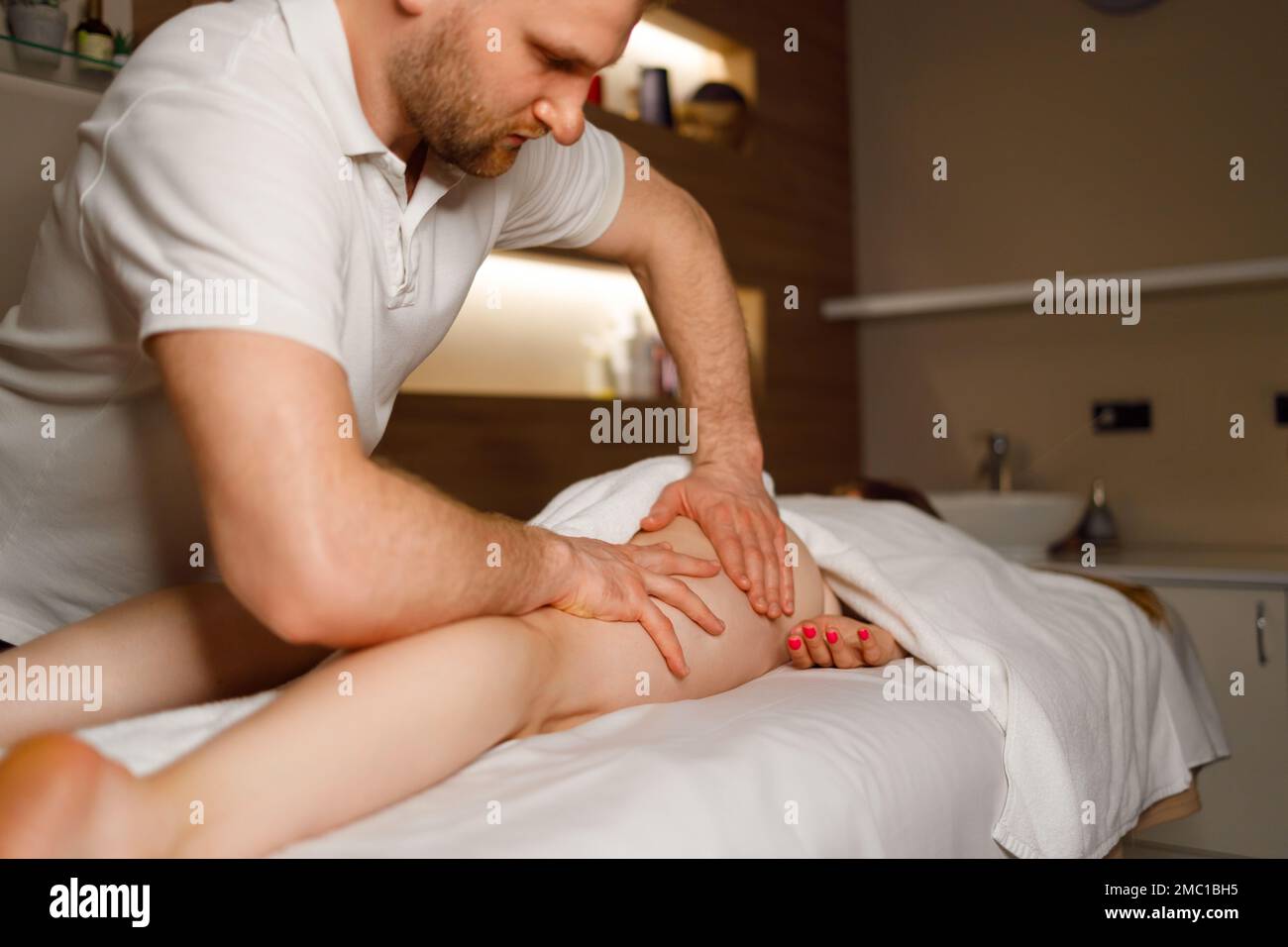 L'uomo forte massaggia le cosce e le natiche di una donna in un salone termale Foto Stock