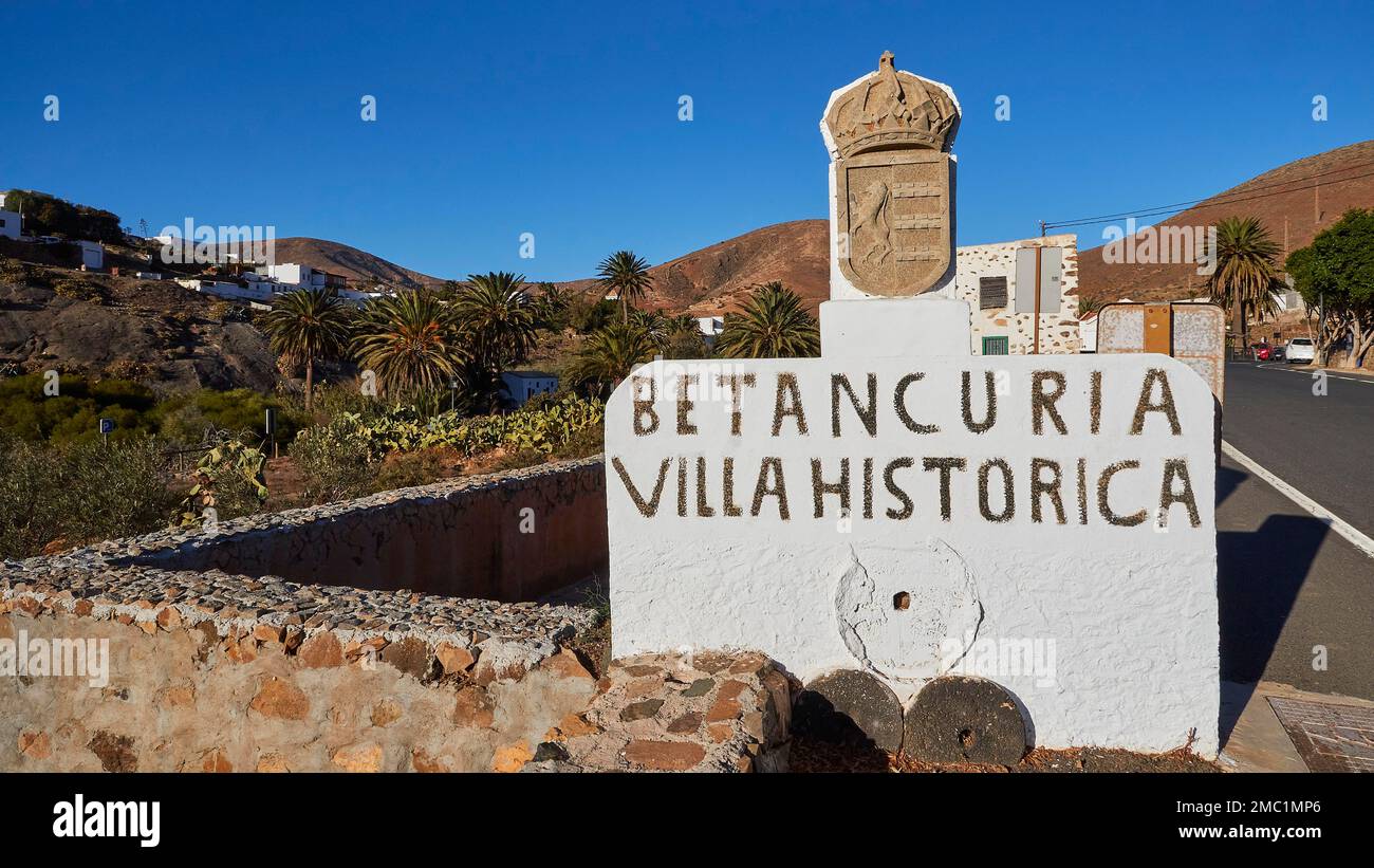 Betancuria, Villa Historica, segno di città in pietra, strada, muraglia bassa, palme, case, cielo azzurro, Fuerteventura, Isole Canarie, Spagna Foto Stock