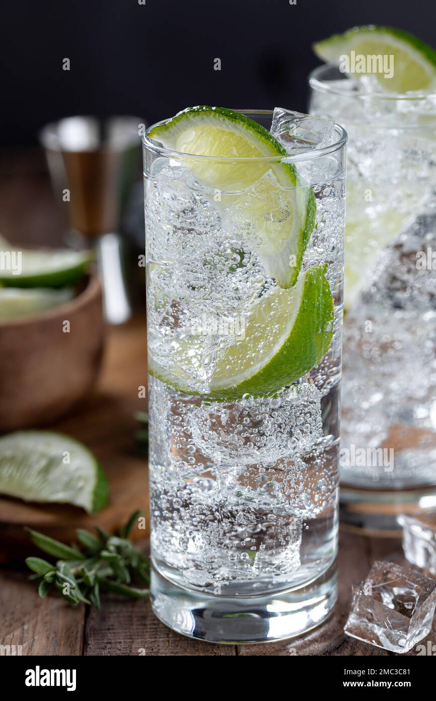 Primo piano di gin e cocktail tonico con fettine di lime e ghiaccio su un tavolo di legno rustico Foto Stock