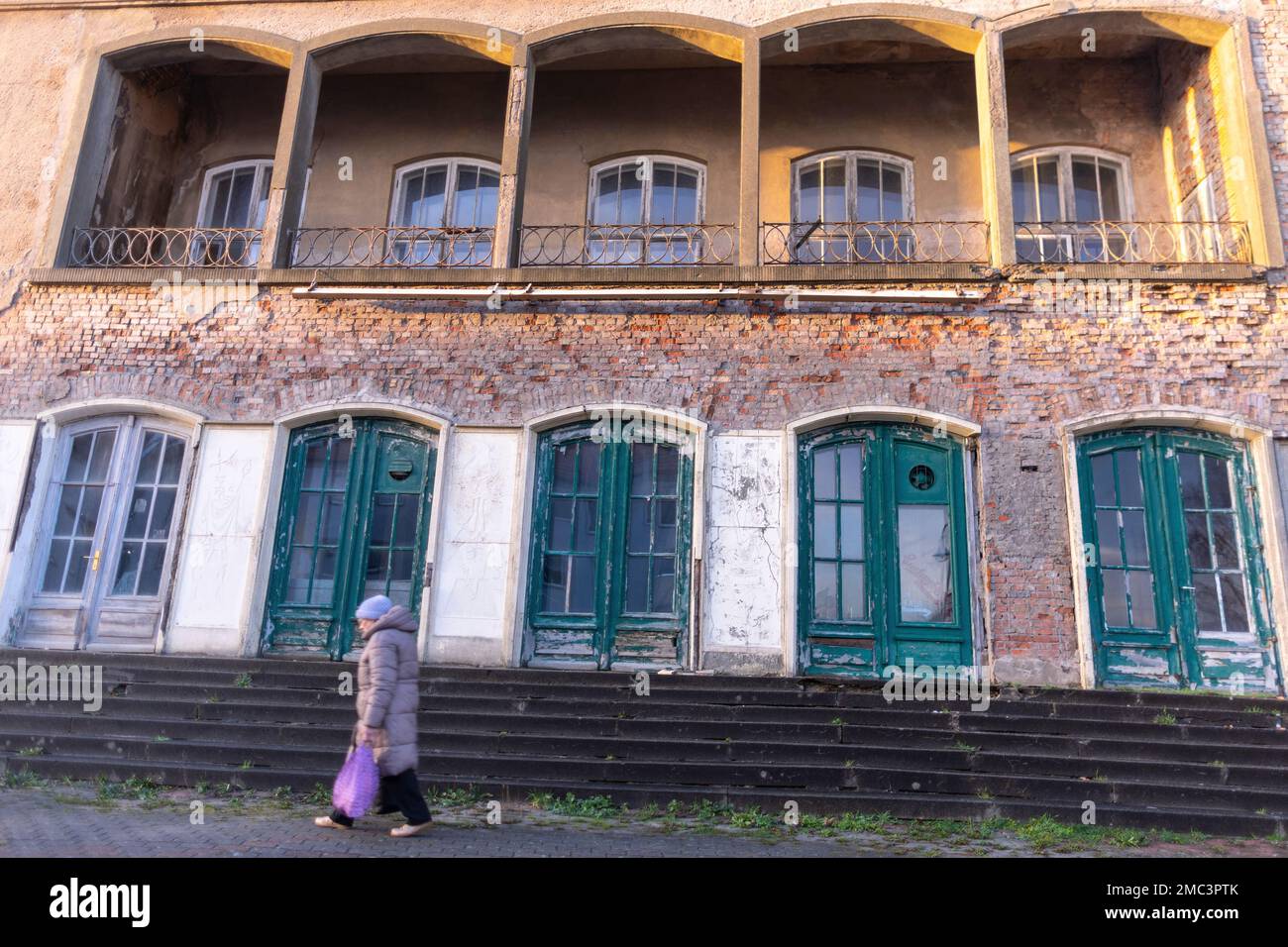 Sassnitz, Germania. 17th Jan, 2023. Una donna anziana passa davanti al centro culturale e al cinema "Haus Stubnitz". (Lunga esposizione) l'edificio nel centro della città è vuoto per anni e continua a deteriorarsi. Secondo l'Ufficio per la conservazione dei monumenti storici, l'edificio sull'isola di Rügen è considerato uno degli ultimi nel suo genere nel Meclemburgo-Pomerania occidentale ed è uno dei più importanti edifici cinematografici conservati del 1950s nel paese. Credit: Jens Büttner/dpa/Alamy Live News Foto Stock