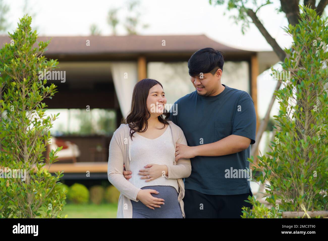 Donna asiatica incinta con suo marito che cammina insieme in giardino a casa per rilassarsi e respirare aria fresca. Foto Stock
