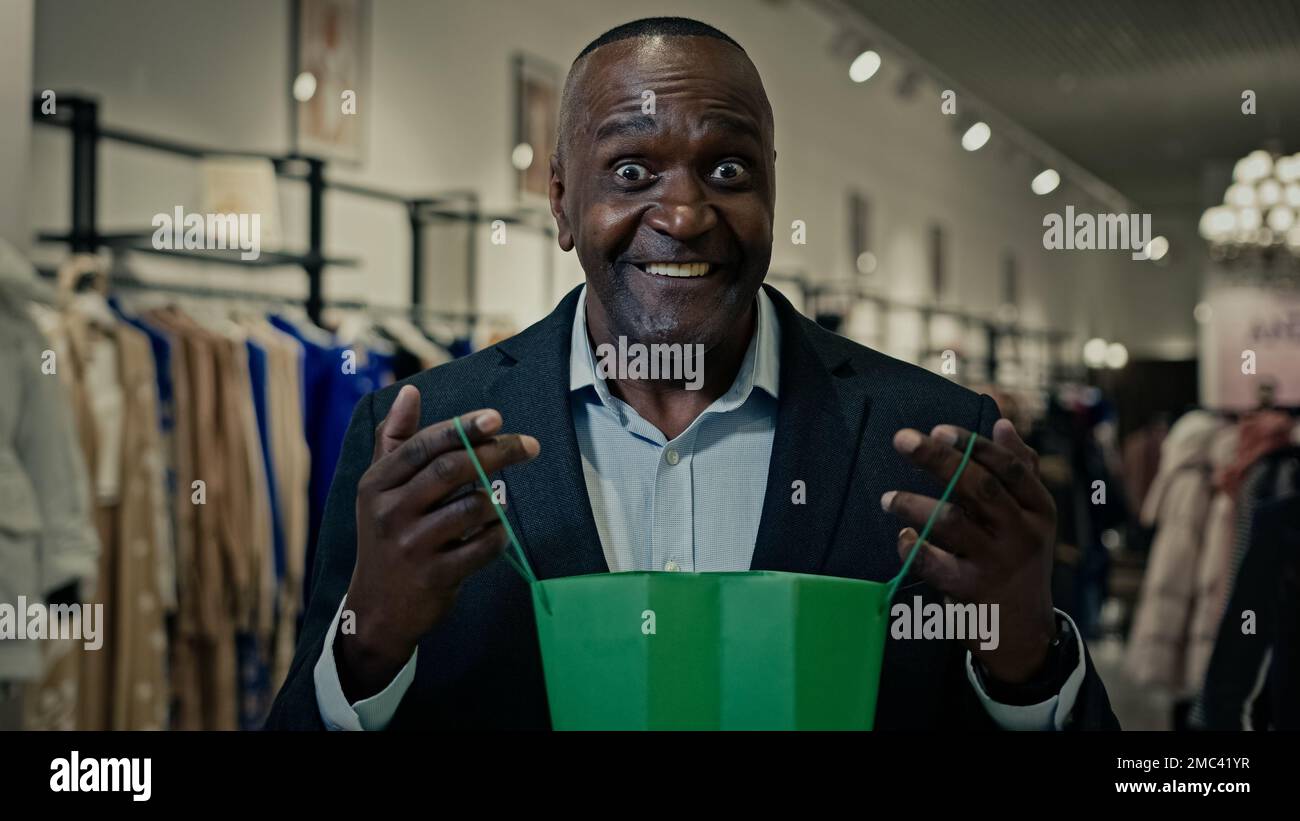 Primo piano uomo africano di mezza età imprenditore uomo americano maschio guardando all'interno shopping bag felice wit pacchetto regalo gioia con presente ricevere ordine Foto Stock