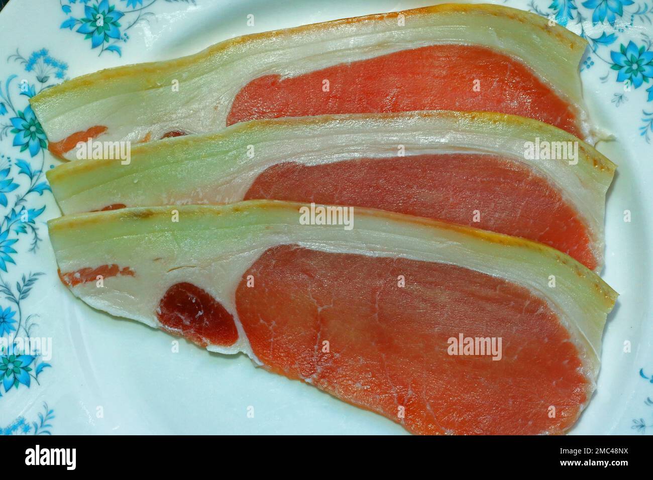 Tre rashers o fette di pancetta cruda di maiale su un piatto pronto per cucinare. Foto Stock