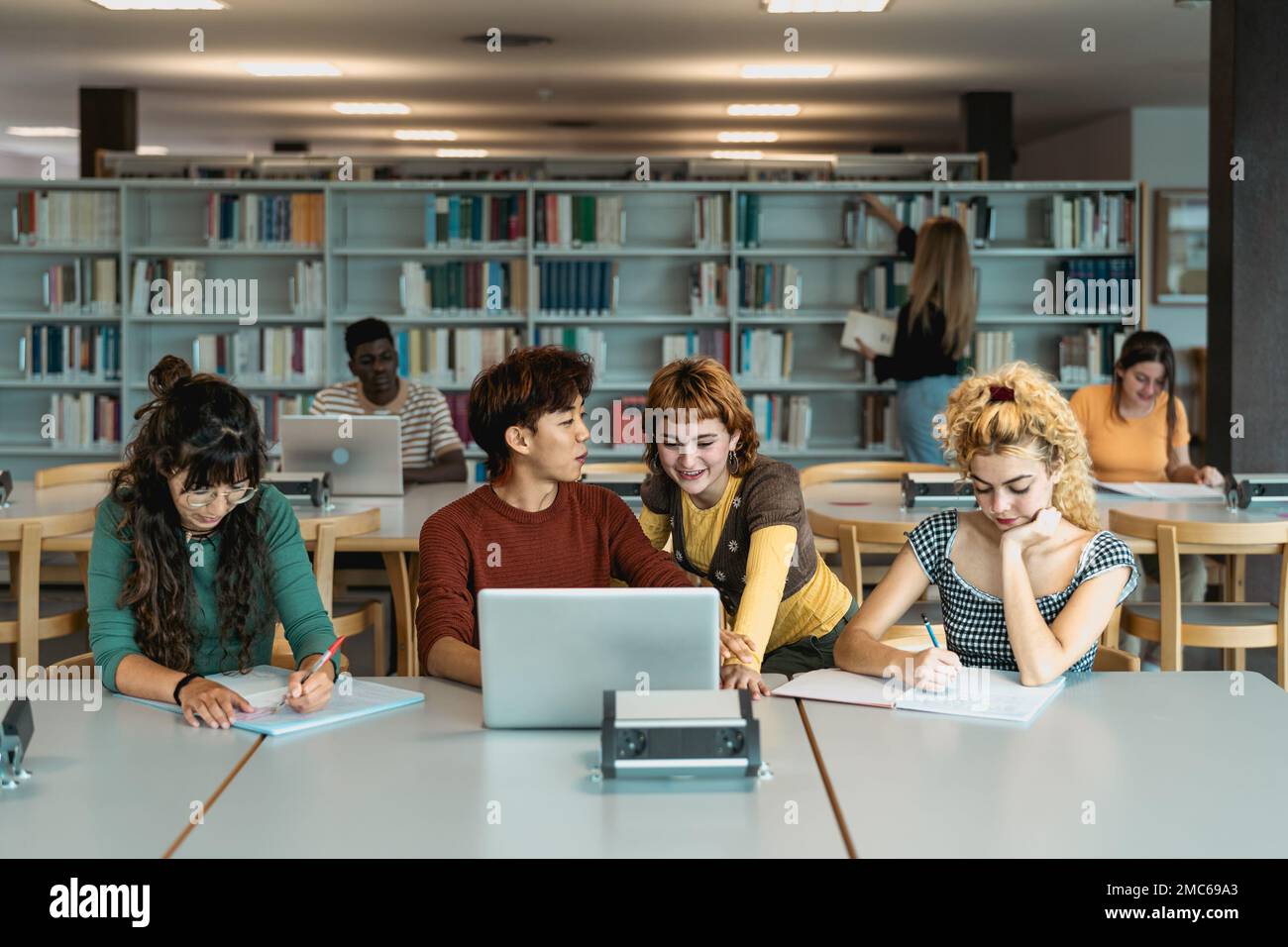 Giovani studenti universitari che usano il computer portatile e studiano con libri in biblioteca - concetto di educazione scolastica Foto Stock