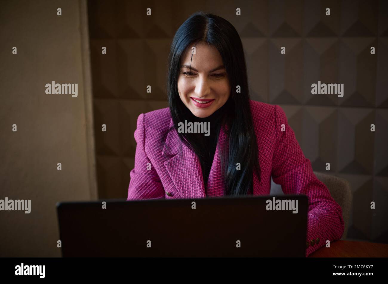 Sorridente imprenditore donna sicuro 40-45 anni, vestito in un elegante giacca cremisi, parlando con i clienti aziendali tramite video link. Entrum. Riuscito Foto Stock