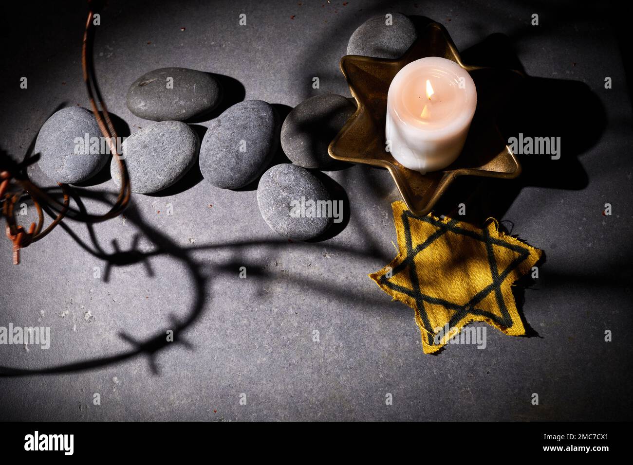 Giorno della memoria dell'Olocausto. Filo spinato, pietre, stella gialla e candela bruciante su sfondo nero Foto Stock