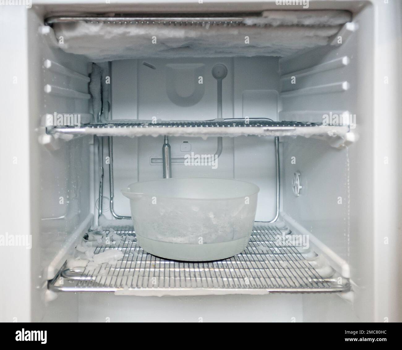 un congelatore aperto molto ghiacciato viene scongelato con una ciotola di acqua calda Foto Stock