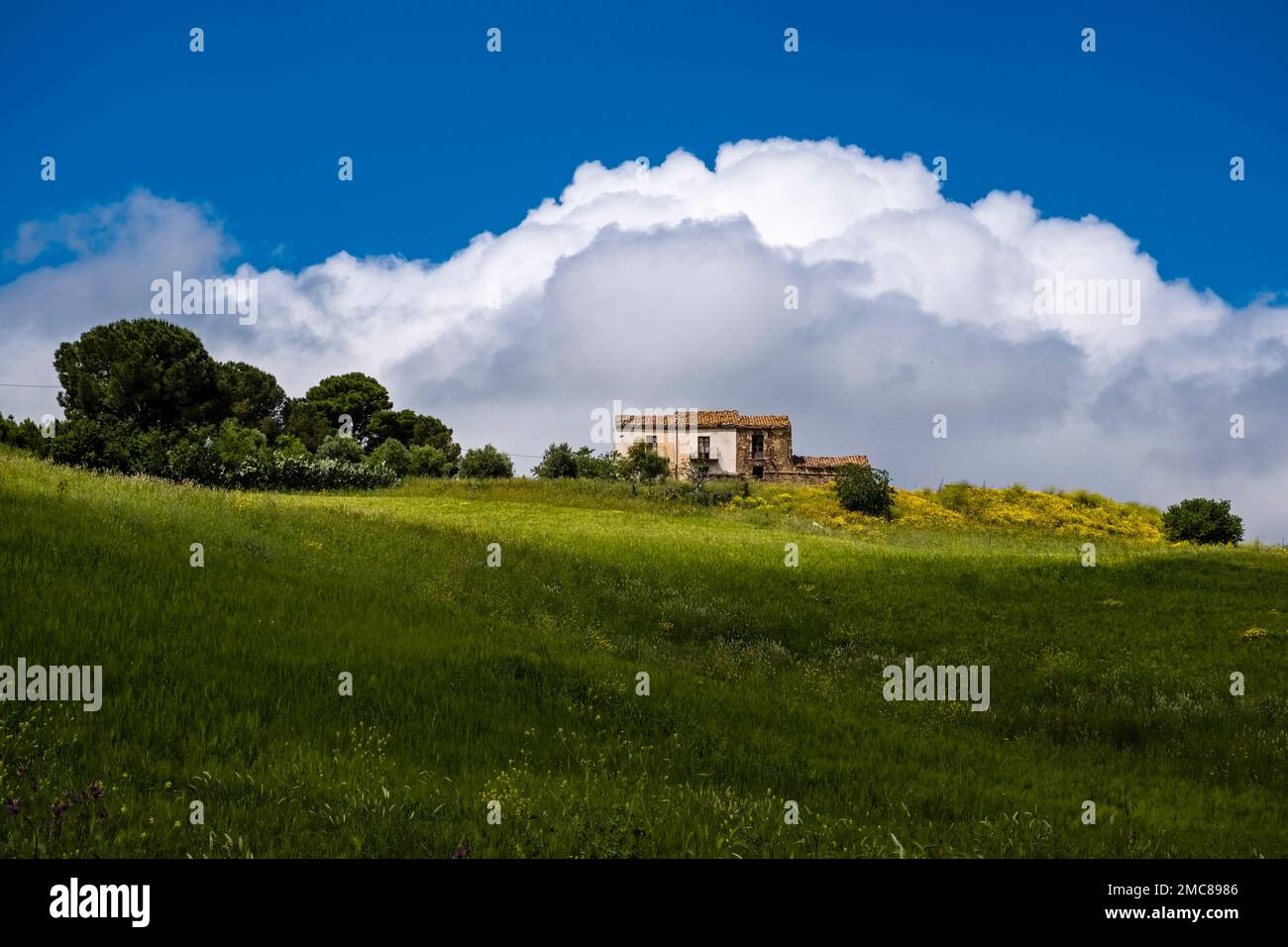 Una casa colonica solitaria su una collina in un paesaggio agricolo siciliano vicino al piccolo paese di Collesano, una nuvola tempesta che si costruisce dietro. Foto Stock