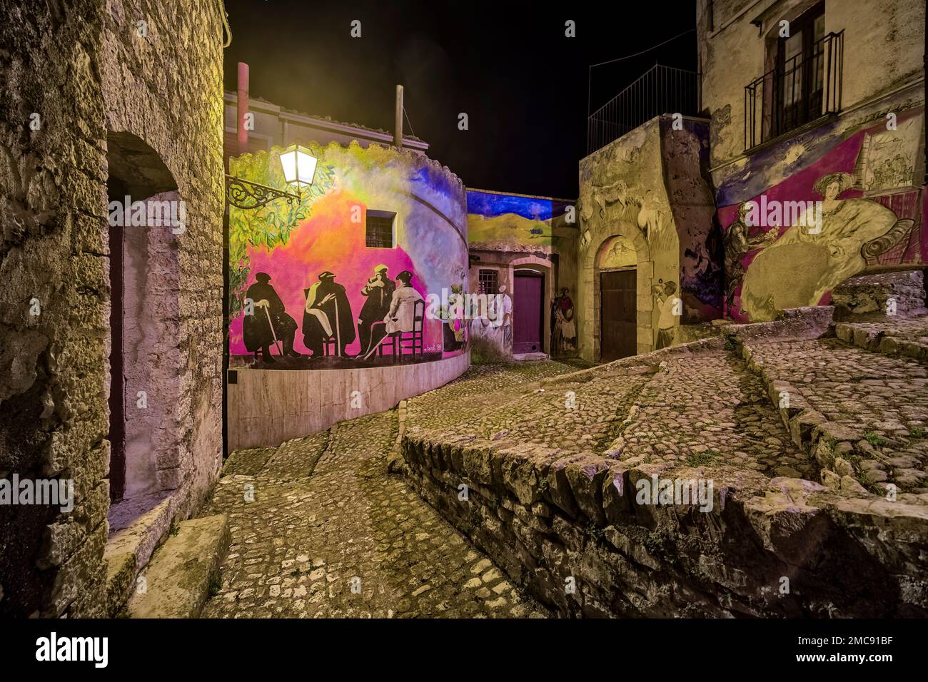 Piccola strada con scalinata, graffiti su un muro e una lanterna nel paese di Prizzi, illuminata di notte. Foto Stock