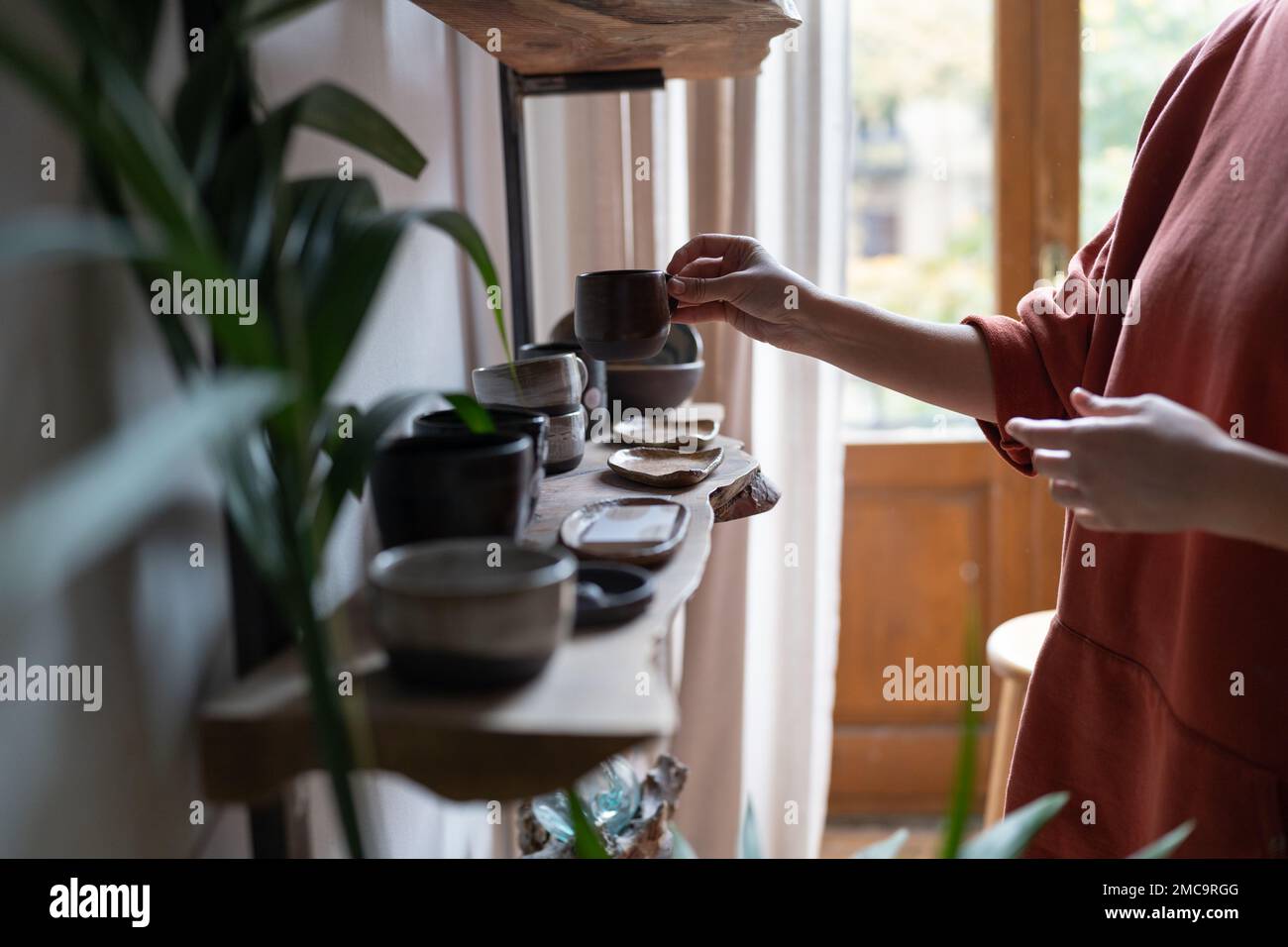 Mani di donna proprietario di negozio di porcellana organizza tazze e piatti su scaffali di legno vetrine Foto Stock