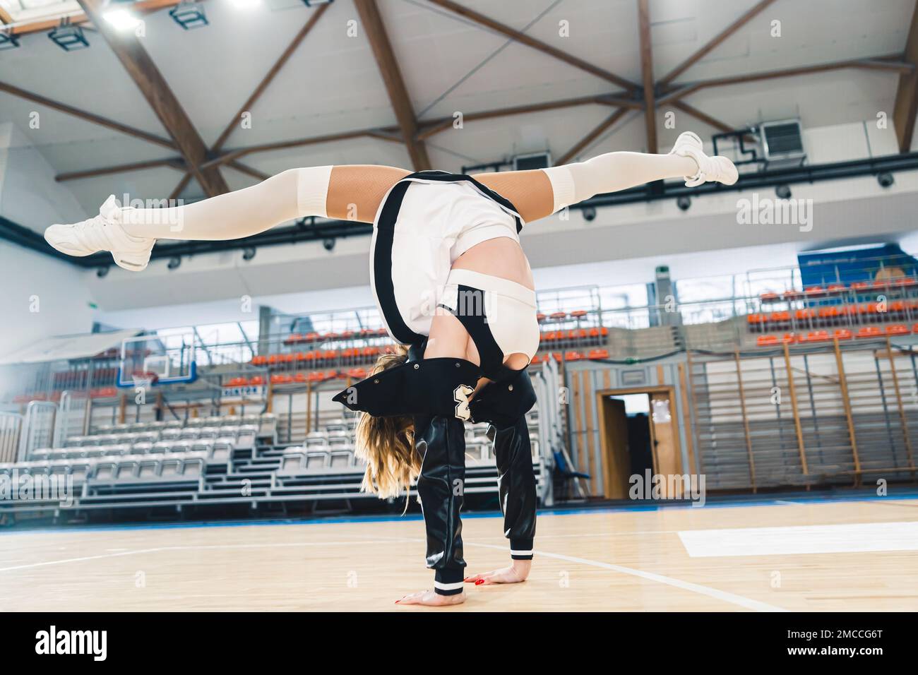 Scatto completo di un cheerleader in stand facendo una spaccatura in una sala sportiva. Gli stand sono sullo sfondo. Foto di alta qualità Foto Stock