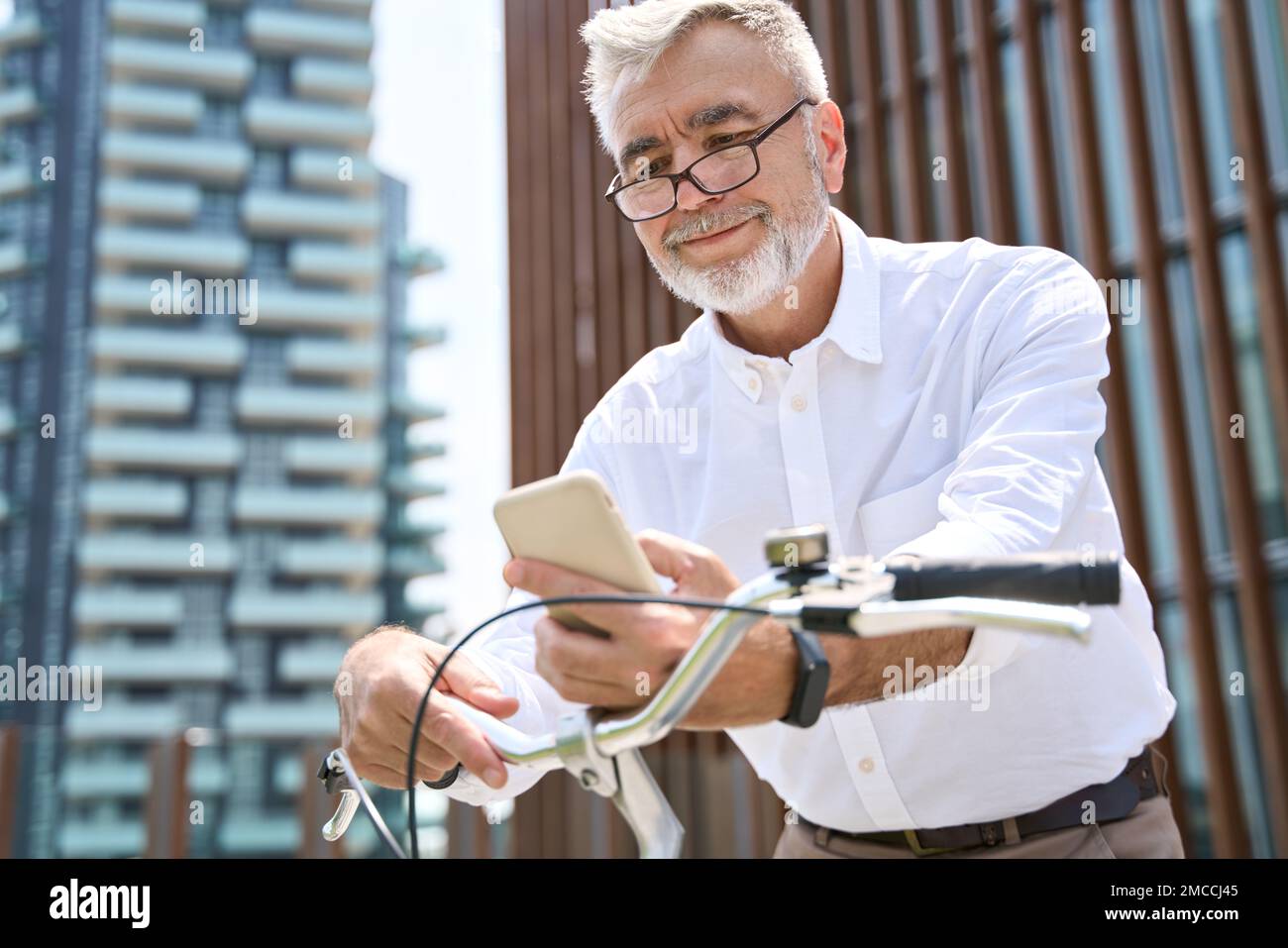 Uomo più anziano attivo che usa il telefono cellulare noleggio bici in app per andare in città. Foto Stock