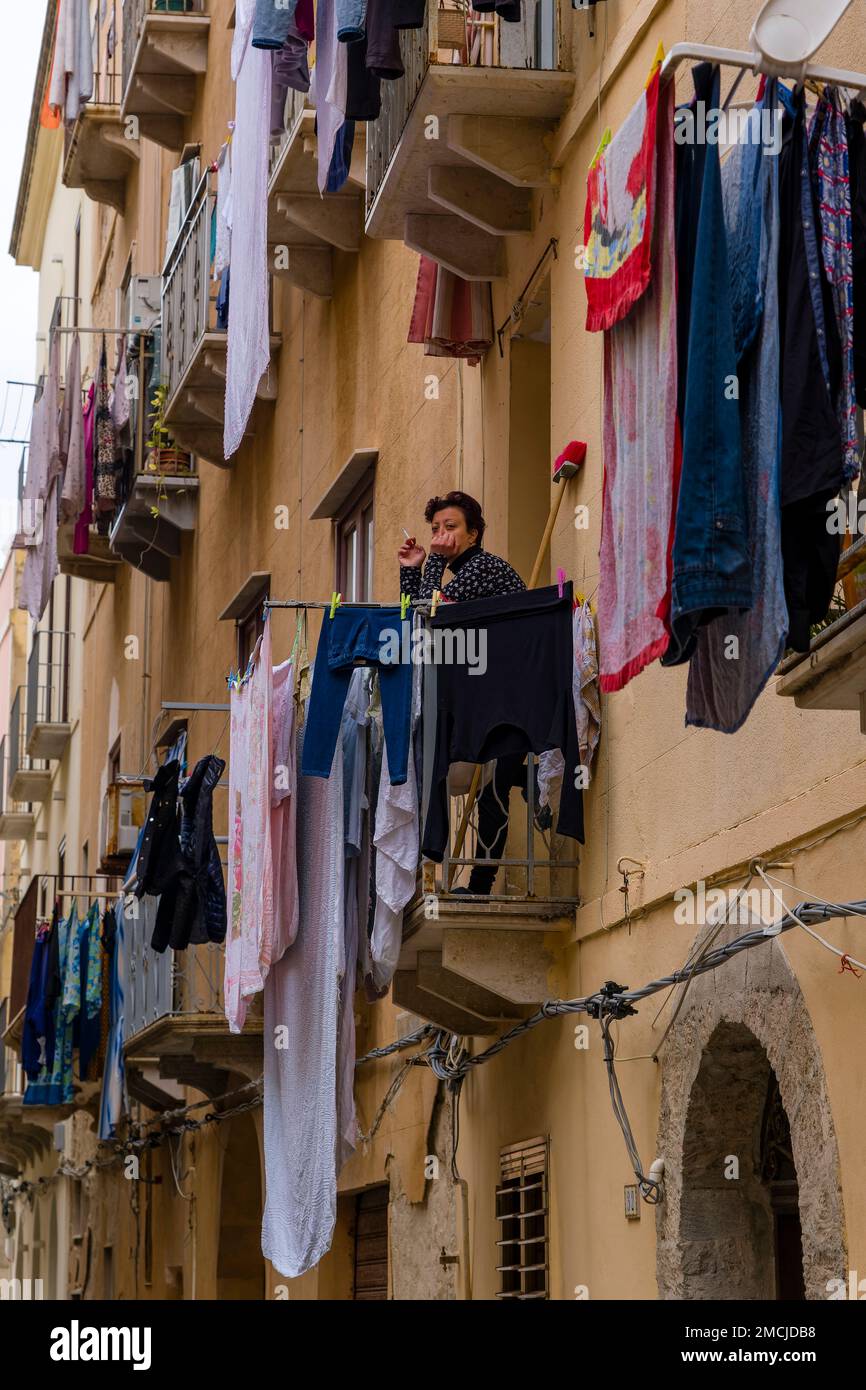 Vicolo stretto di Trapani con balconi, lavanderia appesa e una donna che fuma su un balcone. Foto Stock