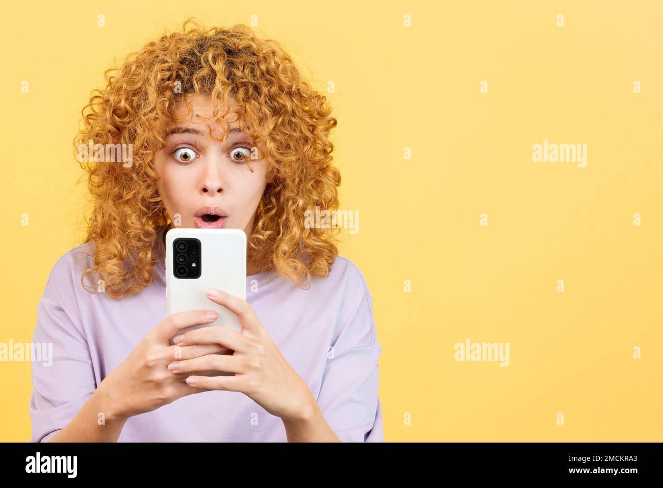 Donna sorpresa con capelli ricci utilizzando il telefono cellulare Foto Stock