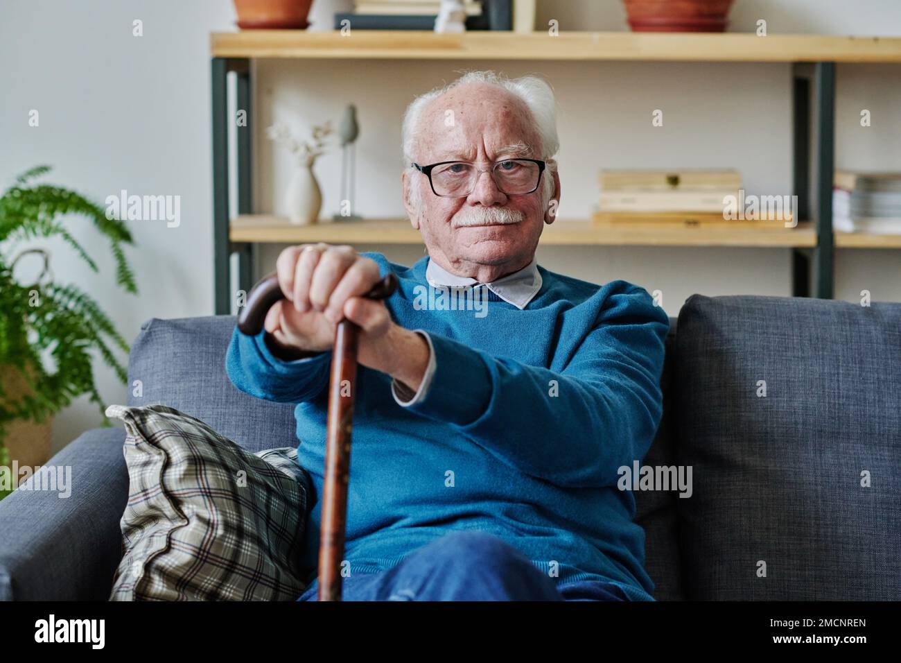 Ritratto dell'uomo anziano con i capelli grigi seduti sul divano nel soggiorno e guardando la macchina fotografica Foto Stock