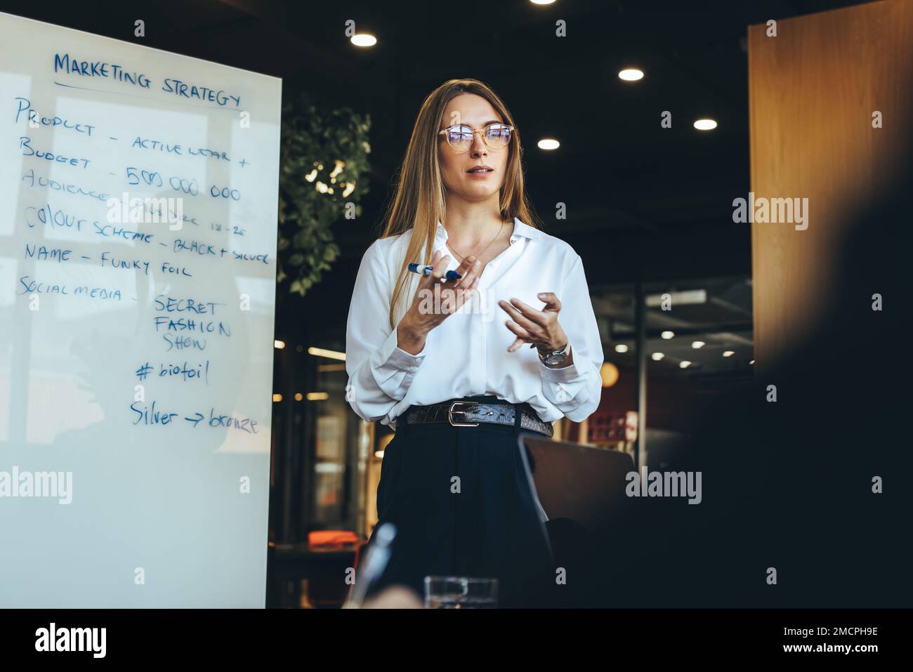 Imprenditrice femminile che discute la sua strategia di marketing con il suo team in un ambiente di lavoro moderno. Fidata giovane donna d'affari che dà una presentazione durante Foto Stock