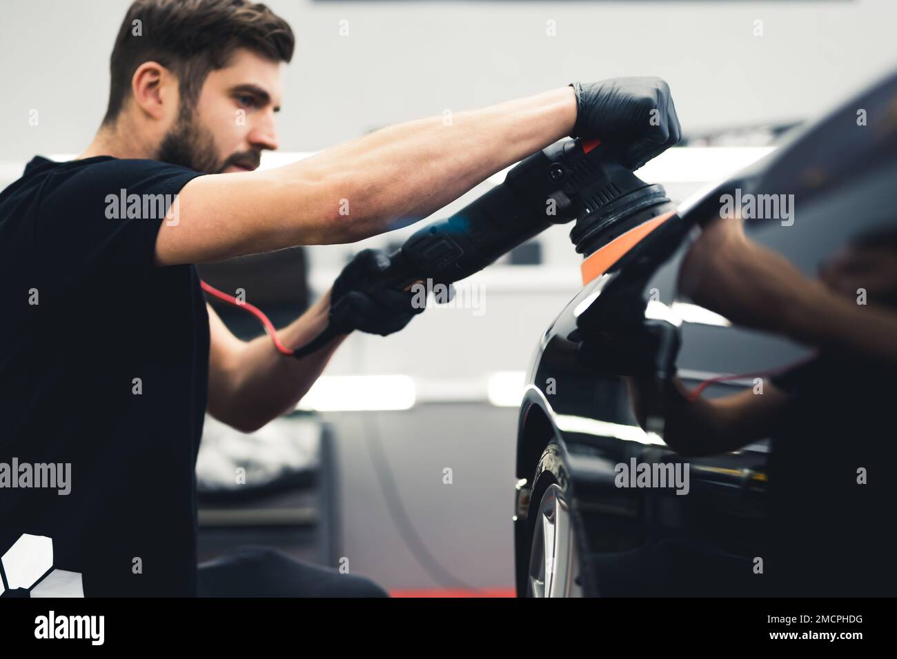 Uomo lucidando vernice nera per auto sportive in studio di dettaglio auto. Verticale laterale. Operaio del collare blu. Foto di alta qualità Foto Stock