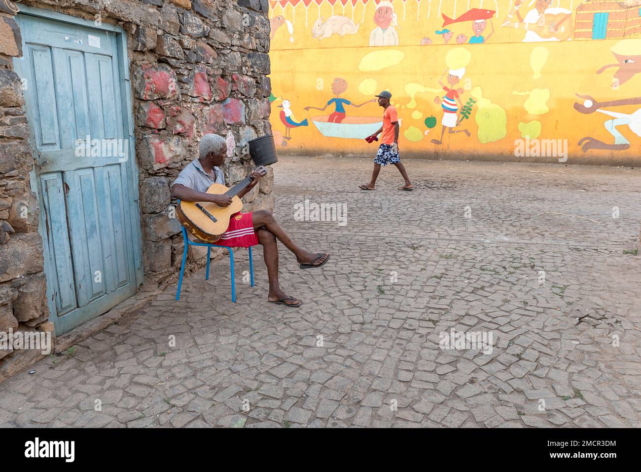 Uomo locale che suona la chitarra di fronte a casa sua in una strada nei quartieri poveri della città di Praia, l'isola di Santiago, Cabo verde Foto Stock
