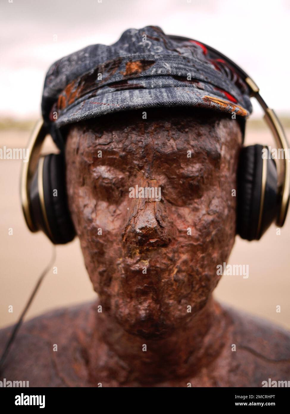 Uno dei personaggi in ferro arrugginiti di Antony Gormley, parte della sua altra installazione artistica, indossa un cappello e delle cuffie. Crosby Beach, Merseyside Foto Stock