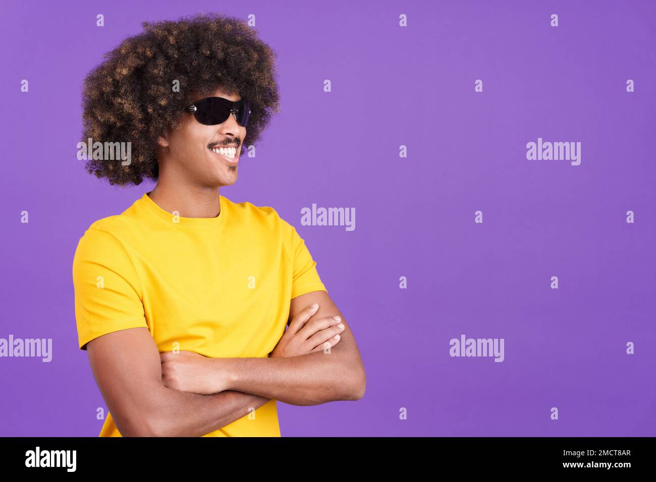 Uomo africano sorridente che indossa occhiali da sole in posa con le braccia incrociate Foto Stock