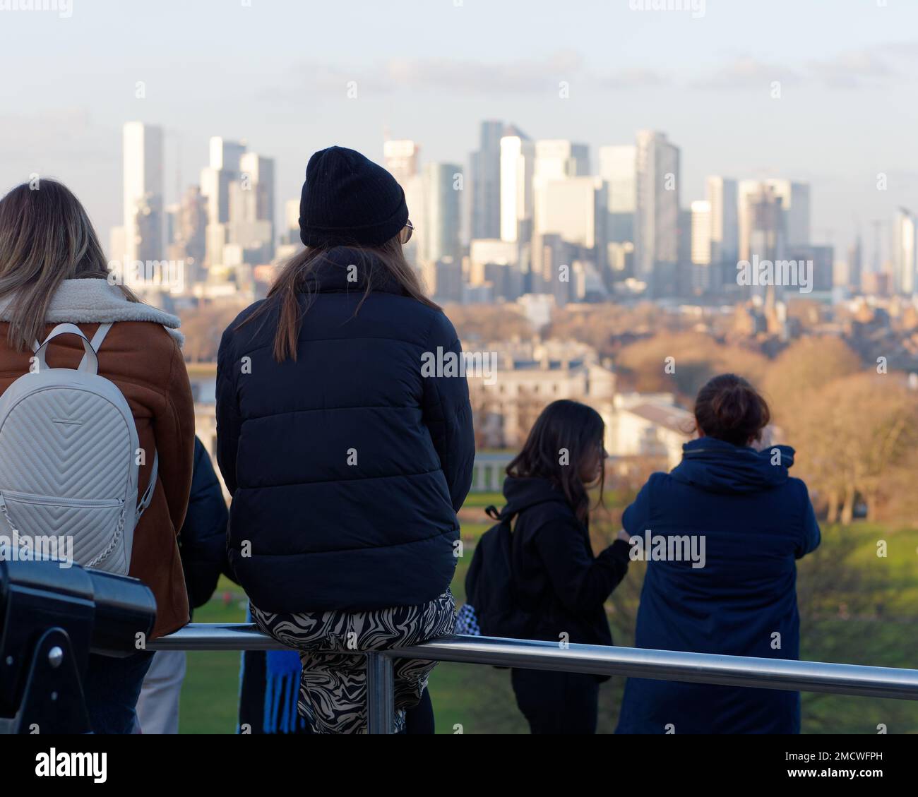 Persone sedute su ringhiere sulla collina di Greenwich Park ammirando la vista verso Canary Wharf. Londra Inghilterra Foto Stock
