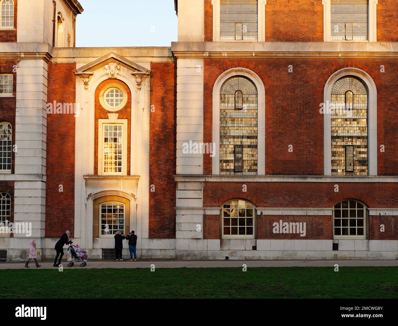 La madre spinge un passeggino davanti agli edifici universitari di Greenwich in un giorno d'inverno, mentre le belle finestre riflettono il sole. Londra Inghilterra Foto Stock