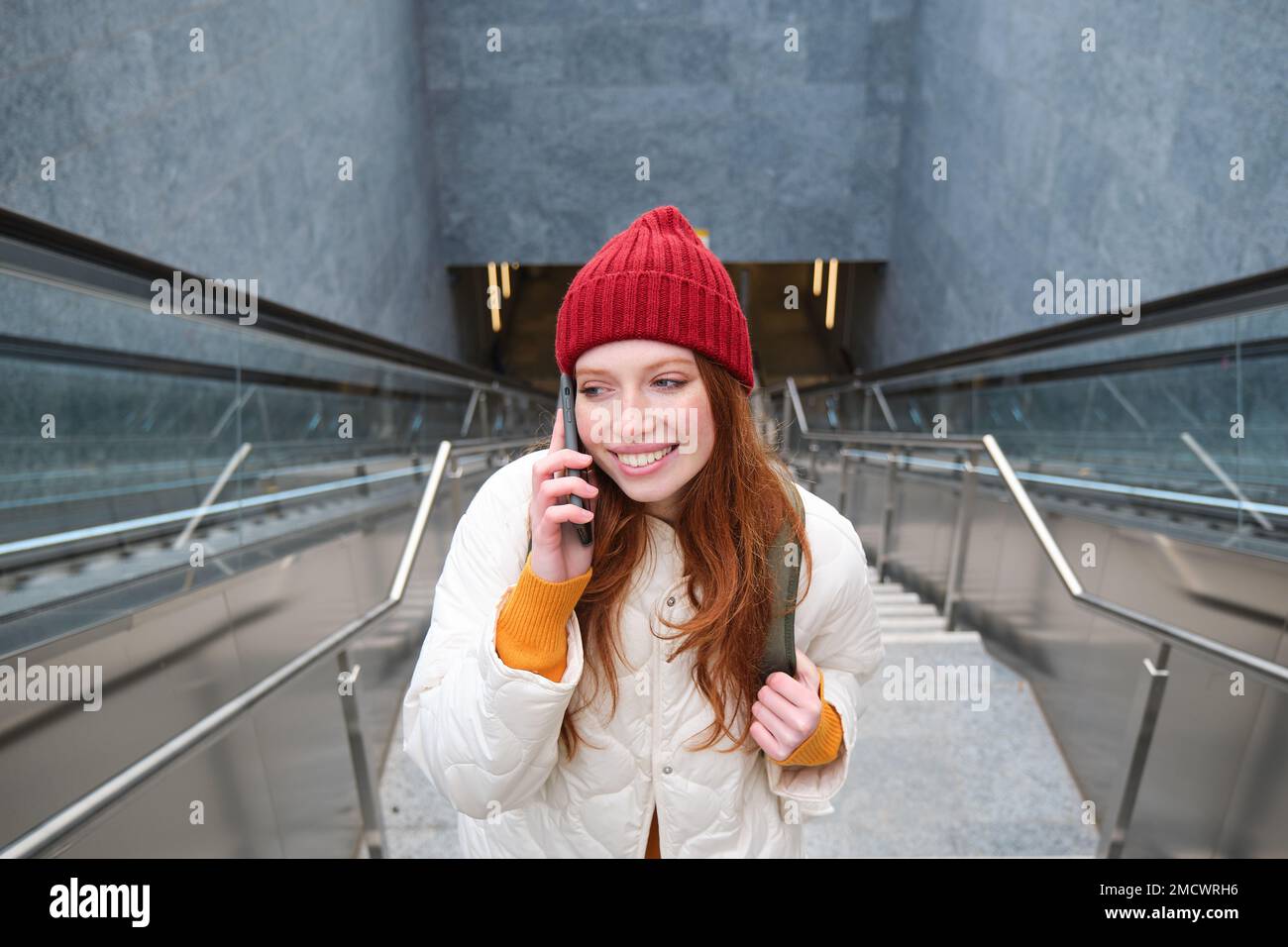 Ritratto di felice donna rossa che cammina per la città con lo smartphone, chiama qualcuno, parla al telefono cellulare all'aperto Foto Stock