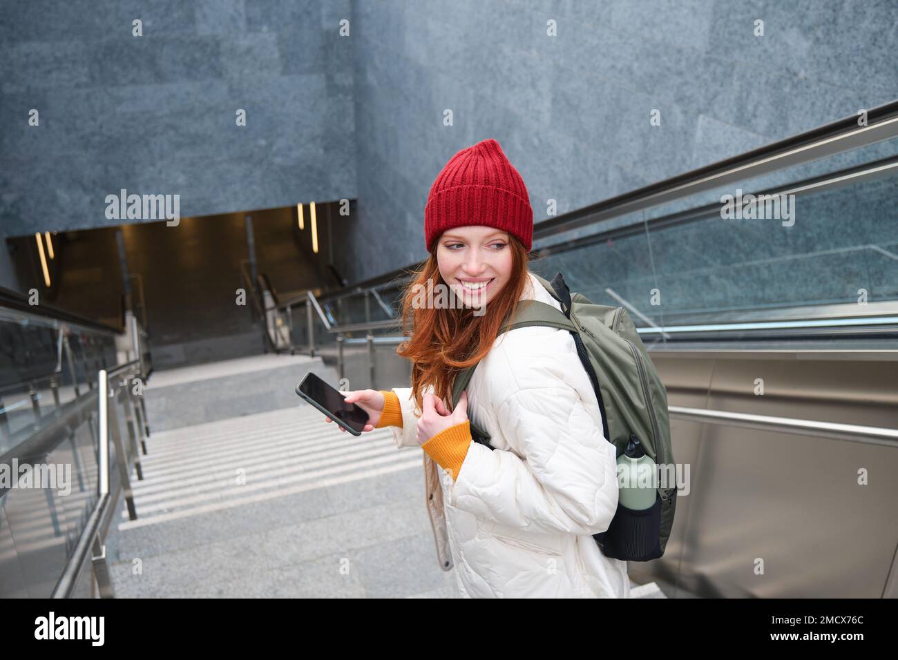 Sorridente ragazza che cammina sulle scale, utilizzando il telefono cellulare, inviando un messaggio via SMS, utilizzando la mappa dell'app per smartphone, segue il percorso verso il luogo di destinazione Foto Stock