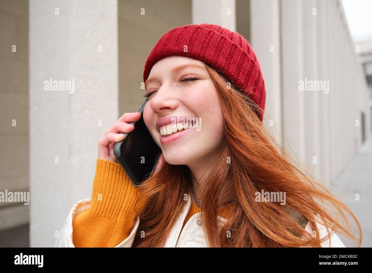 Banda larga mobile e persone. Sorridente giovane donna rossa cammina in città e parla sul telefono cellulare, chiamando un amico su smartphone, utilizzando internet per fare Foto Stock