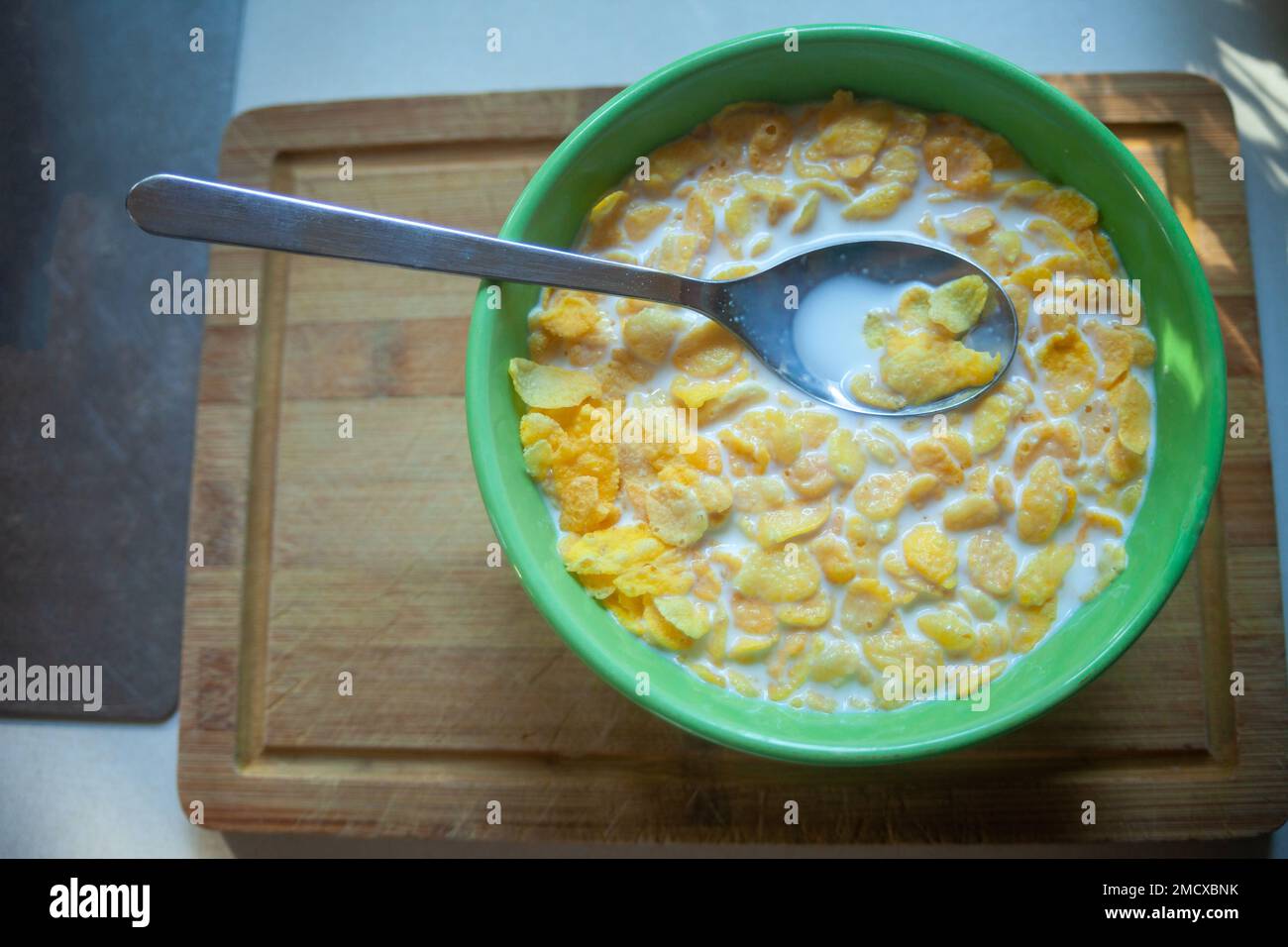 Corn flakes con latte in un recipiente verde con cucchiaio, vista dall'alto Foto Stock