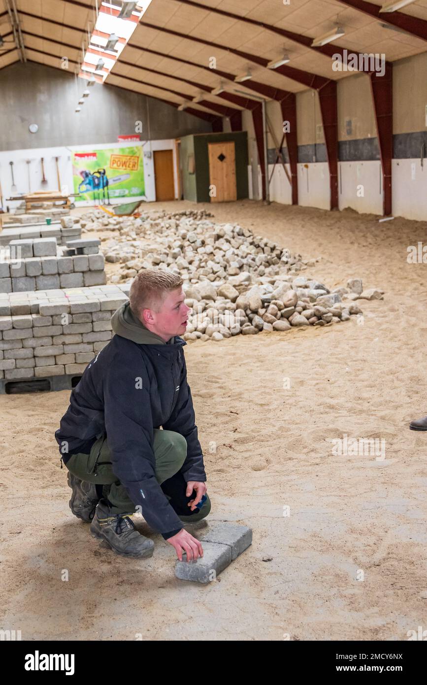 Aarhus, Danimarca - 16 novembre 2022: Studente che presenta la sala di istruzione di una scuola professionale con mucchi di mattoni per tutti i tipi di istruzioni pratiche di pavimentazione e di formazione Foto Stock