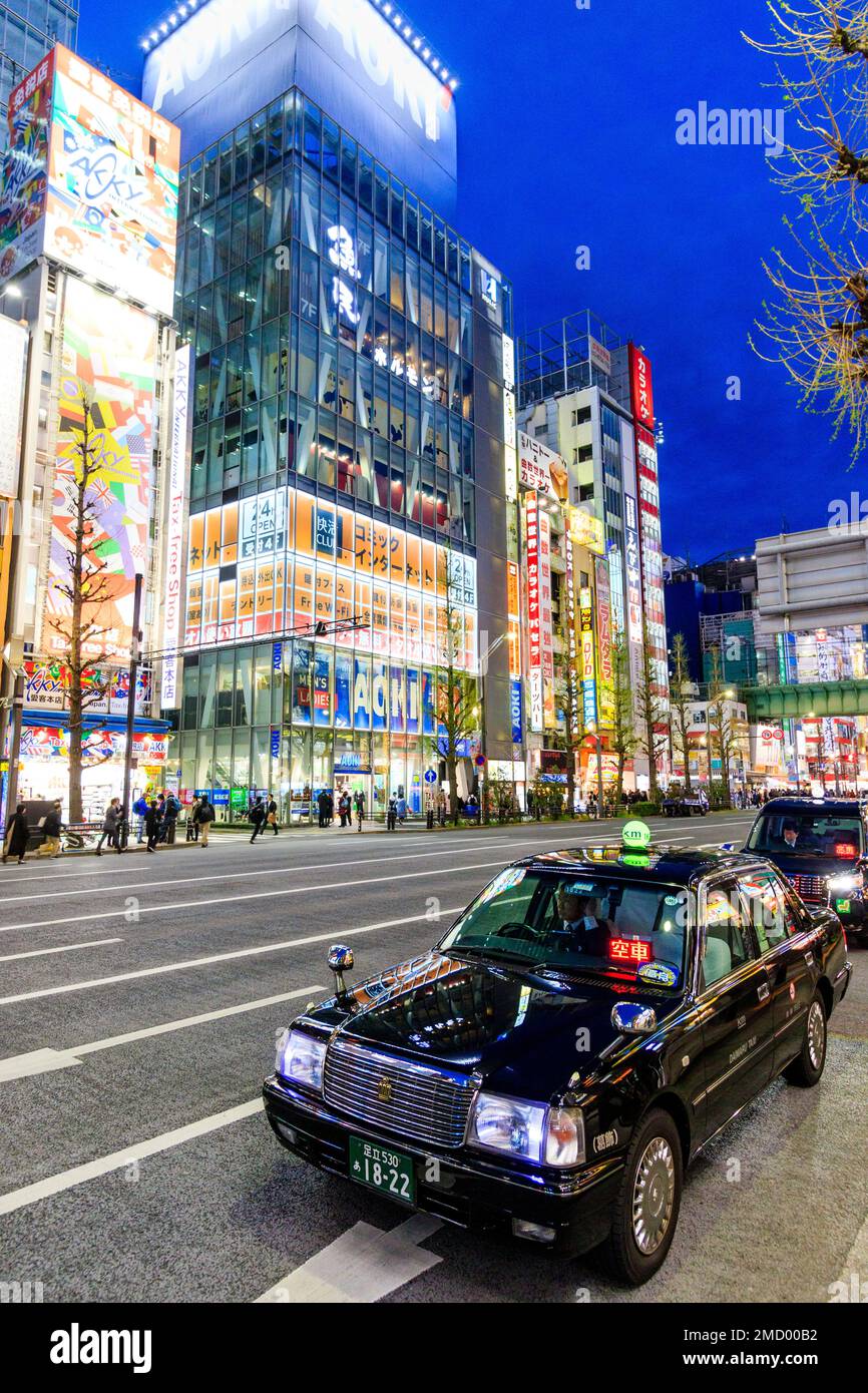 Tokyo, Akihabara. Chuo Dori, la principale strada dello shopping. Due taxi in attesa in primo piano, strada da attraversare vari negozi illuminati e segni. Notte tempo. Foto Stock