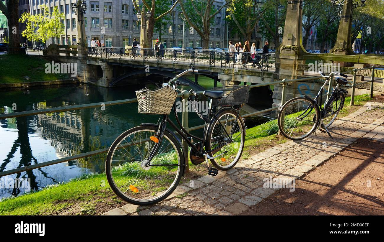 Königsallee non è solo un famoso viale commerciale di Düsseldorf, ma ha anche aree verdi con alberi antichi. Biciclette parcheggiate presso il canale della città 'Kö-Graben'. Foto Stock