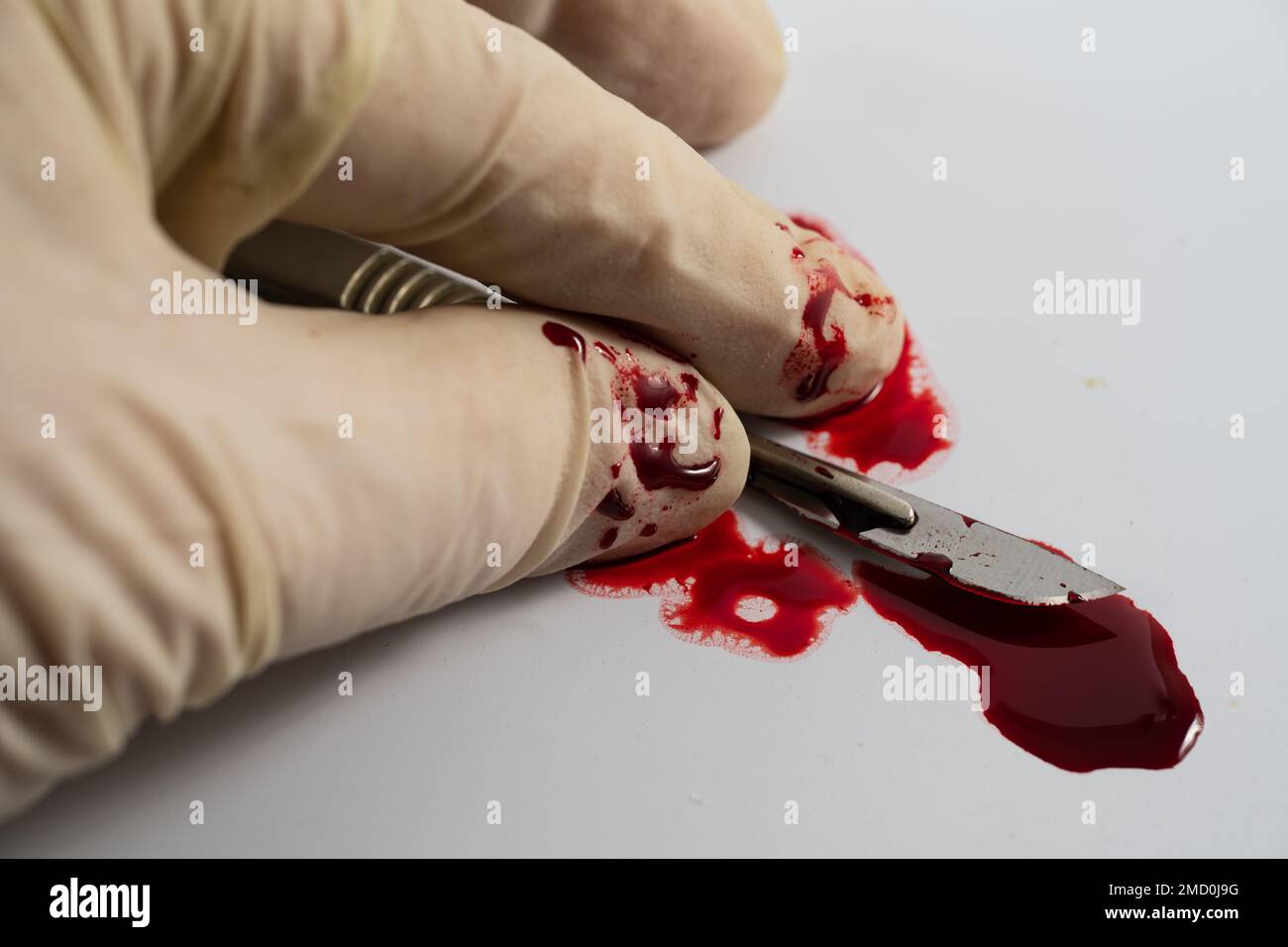 lama sterile in acciaio inox colorato con sangue e guanto in lattice salute chirurghi professionali bisturi isolato su uno sfondo bianco con piscina di sangue Foto Stock