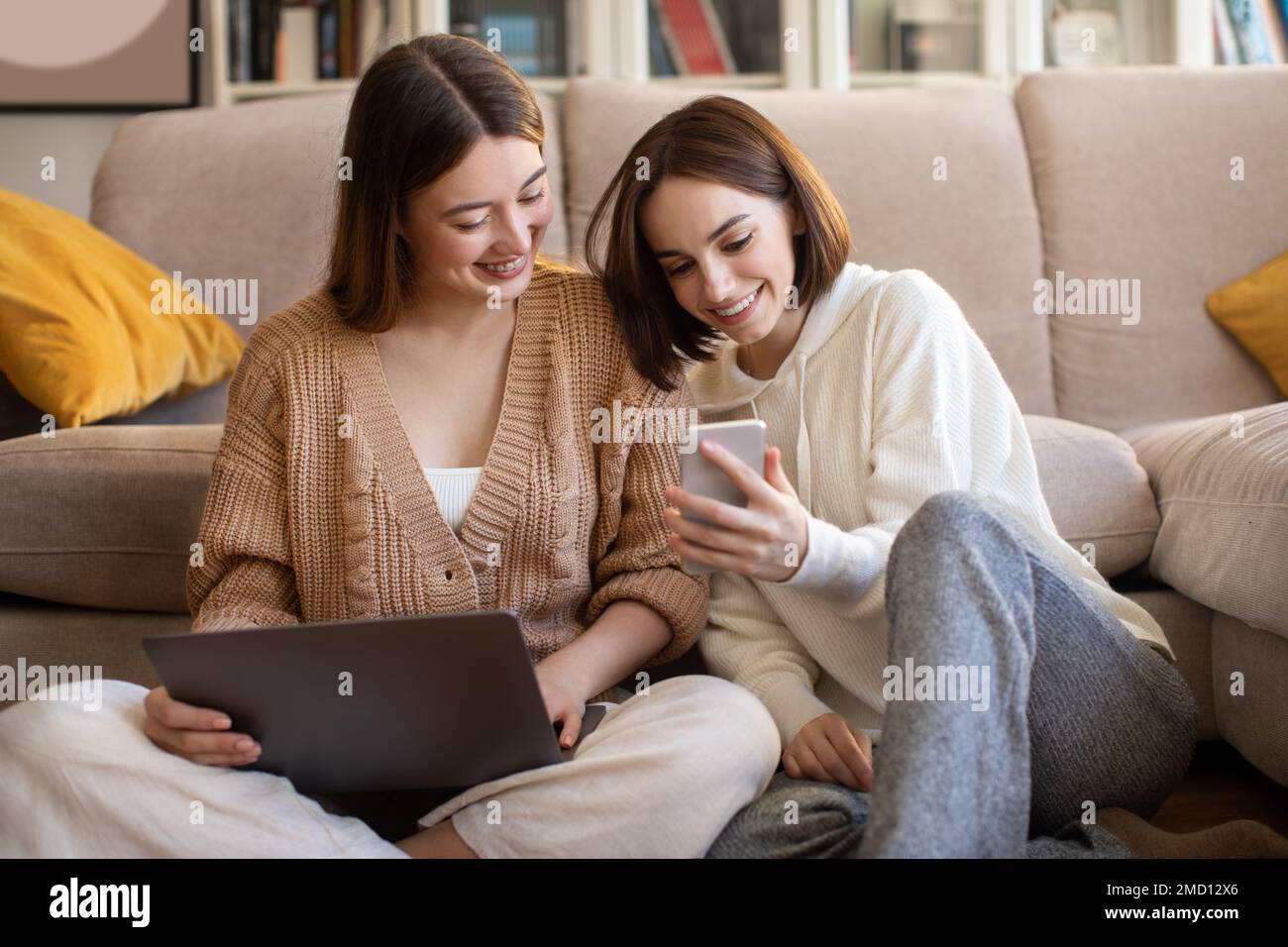 Giovani donne europee sorridenti con laptop e smartphone che navigano in internet, chattano, mostrano video Foto Stock