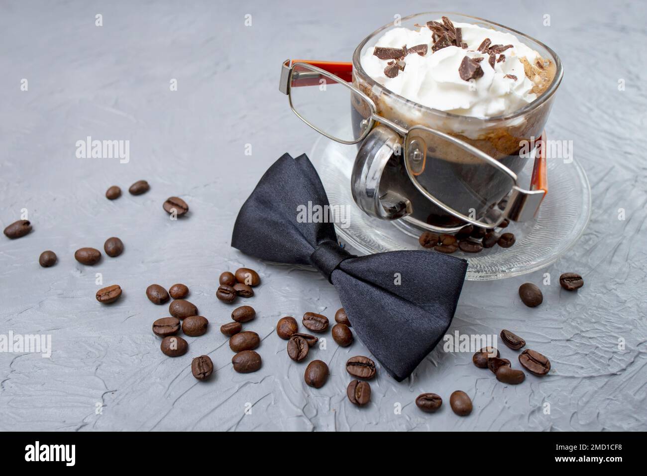 Bicchiere di caffè con panna montata e chicchi di caffè. Caffè, cravatta e occhiali con texture grigio cemento. Foto Stock