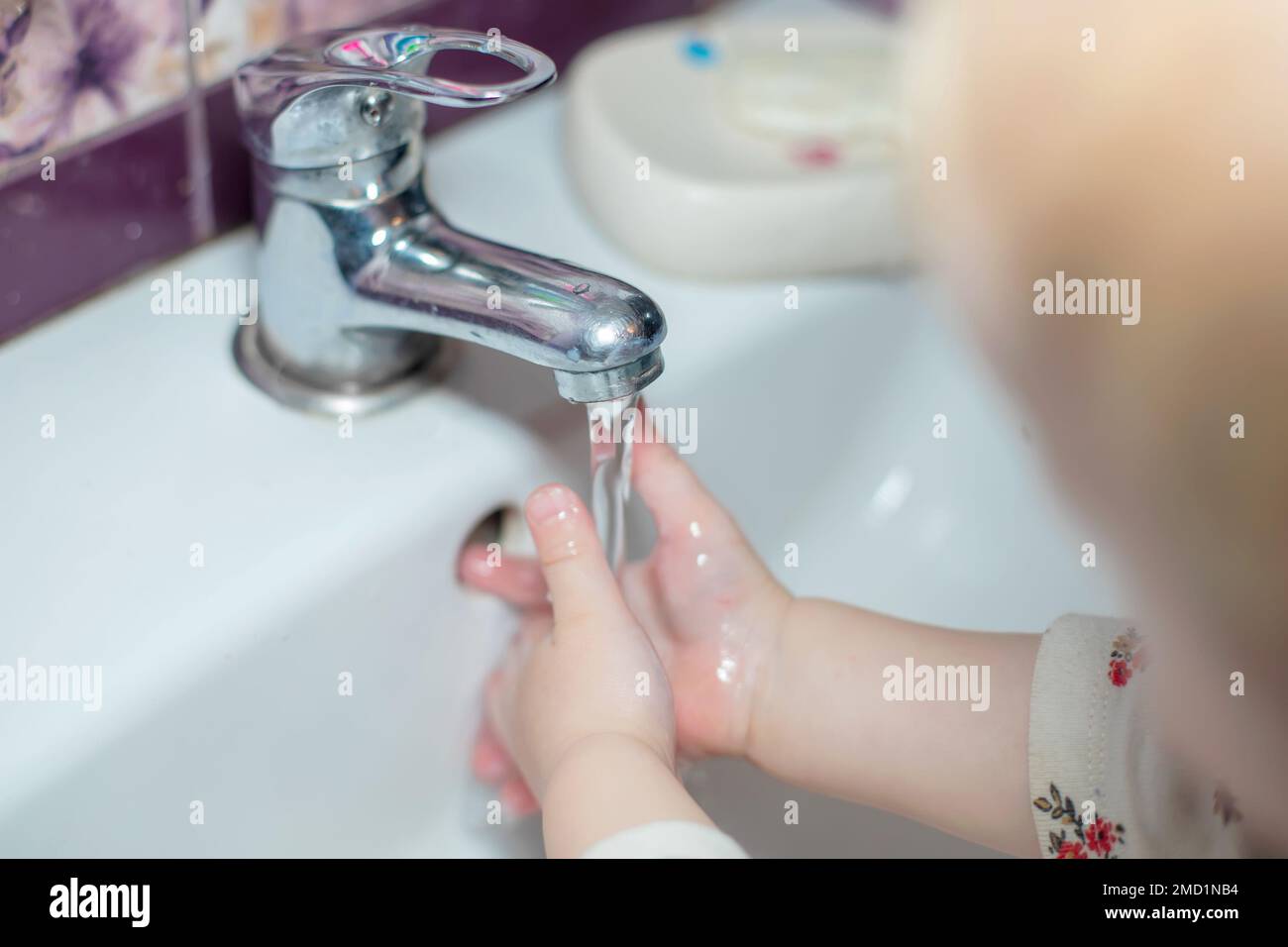 il bambino mette le mani sotto il flusso d'acqua del rubinetto. Risparmio di acqua. Pulizia della mano per fermare la diffusione di Covid-19, pandemia di Coronavirus Foto Stock