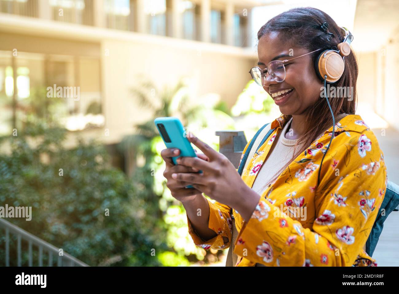 Donna sorridente che parla al suo smartphone con cuffie e zaino all'università - felice giovane studente hipster ascoltare la musica e guardare il Foto Stock