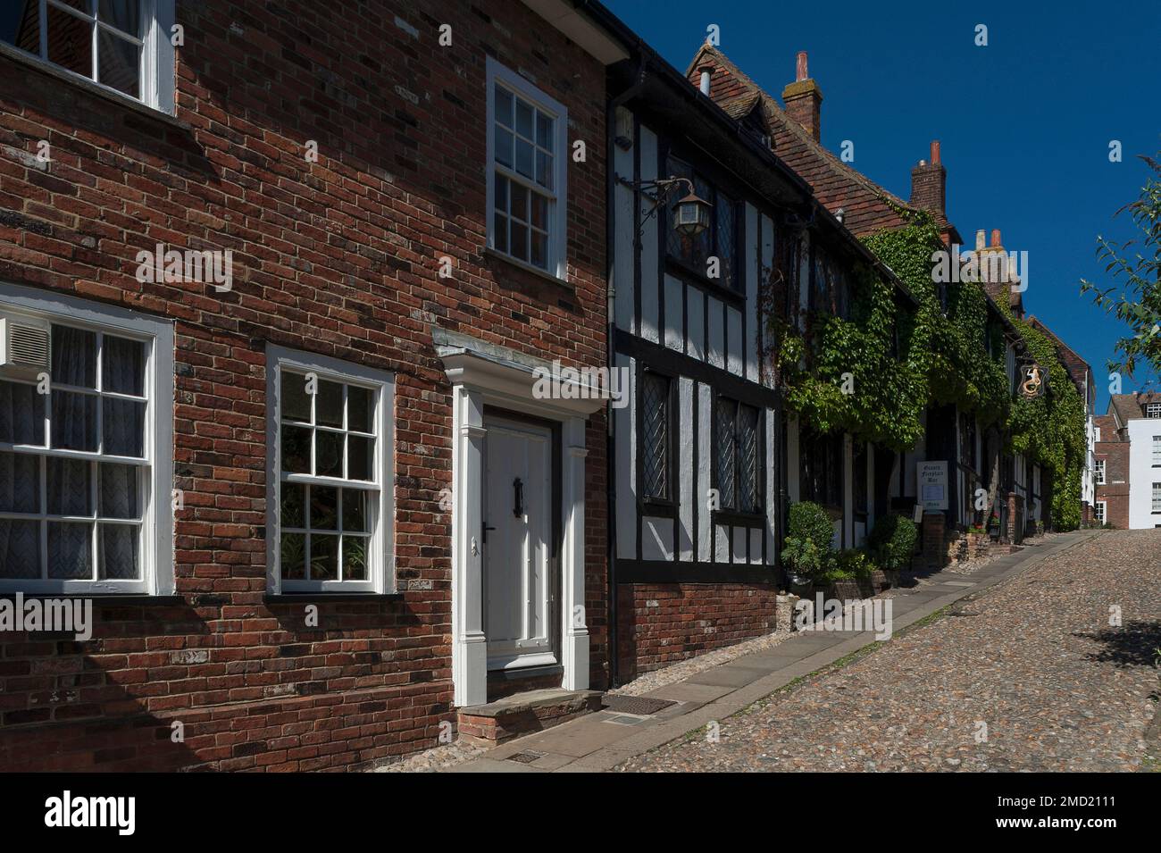 Una sirena d'oro contro foglie verdi e antiche strutture in legno: Inn segno della sirena Inn, ricostruita nel 1420, è appesa da elaborate opere in ferro battuto sopra la superficie acciottolata di ripida-salita Mermaid Street nel cuore di Rye, Sussex orientale, Inghilterra, Regno Unito. Foto Stock