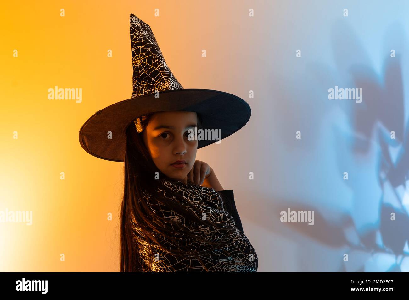 Una strega giovane e graziosa. Festa di Halloween. Ritratto di una ragazza adolescente carina in posa in studio in costume di una strega e una bacchetta magica in mano. Misto Foto Stock