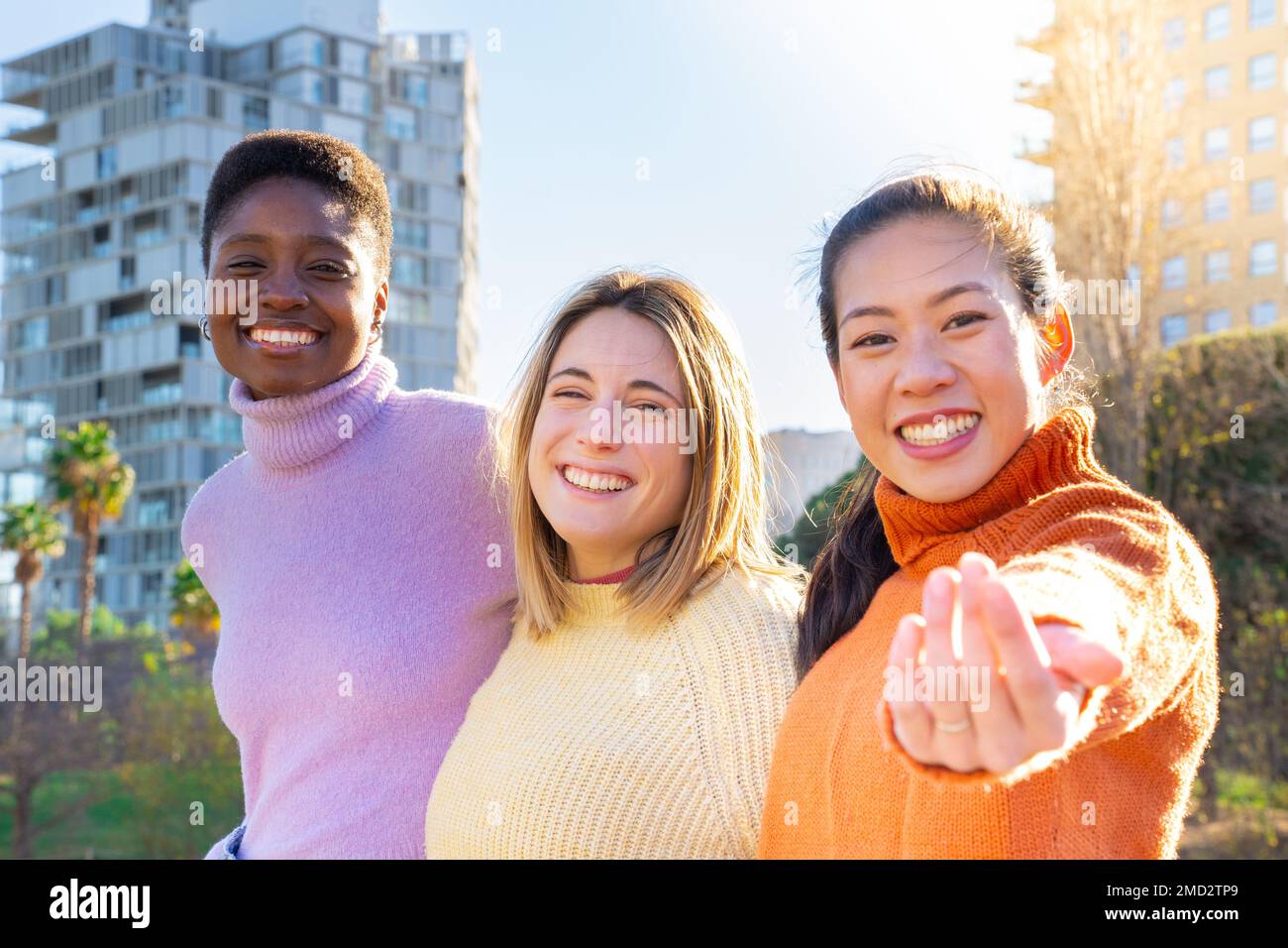 Ritratto di alcuni amici che si abbracciano affettuosamente guardando la fotocamera accogliente con la mano. Ragazze che si divertono in città. Autentico Foto Stock
