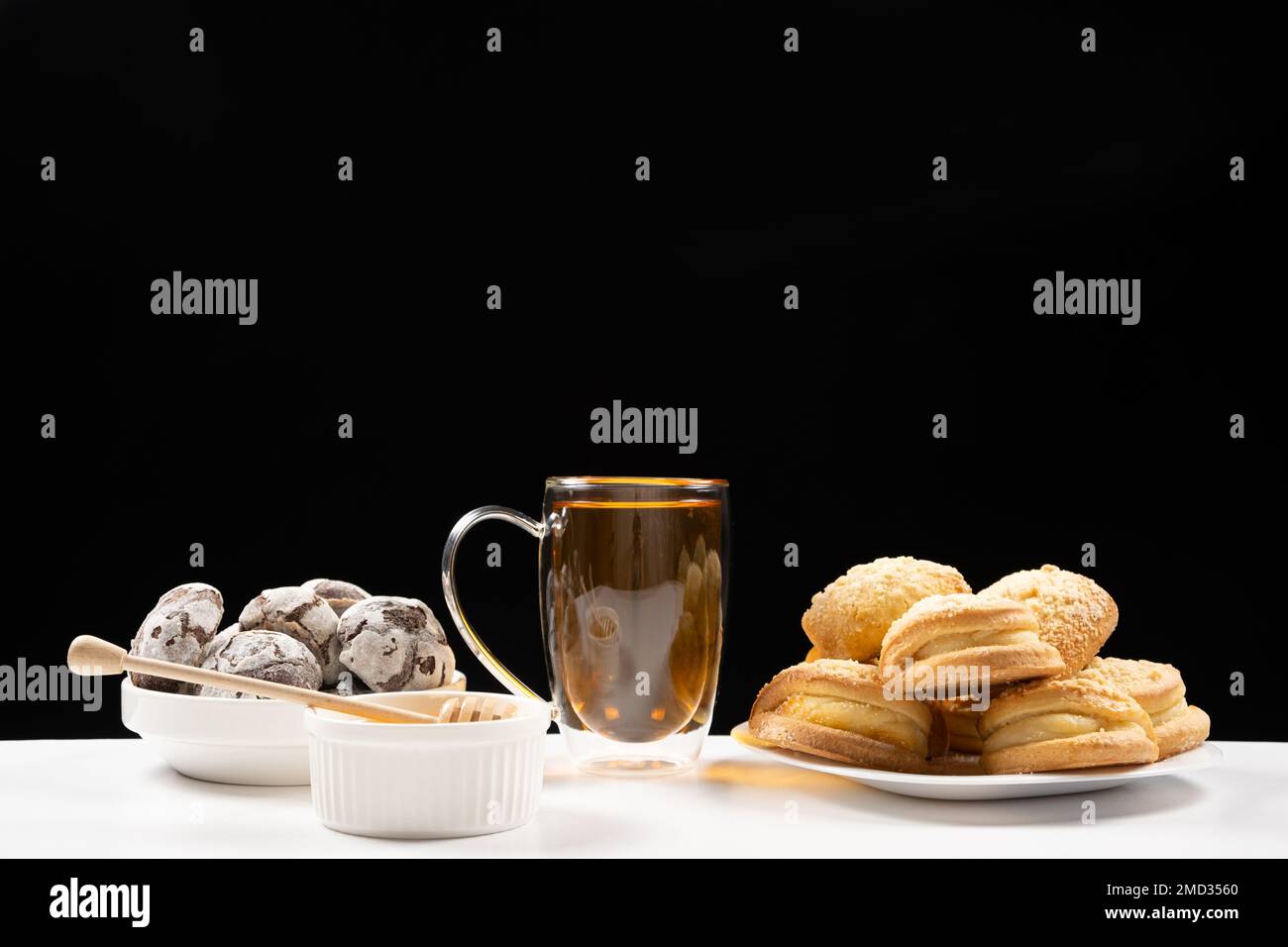 Tè al miele con biscotti al cacao e torte con farcitura cremosa su fondo nero. Foto Stock