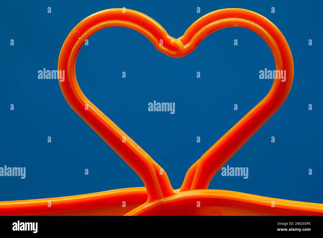 Un cuore per i vestiti. Due ganci in plastica arancione su sfondo blu che si combinano per formare una forma a cuore. Foto Stock
