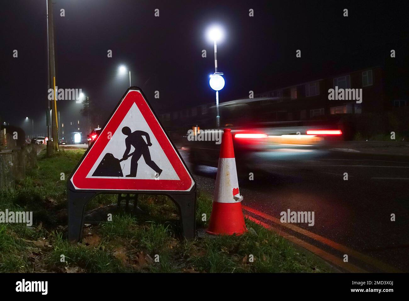 Un segnale triangolare per i lavori stradali e un cono stradale sul lato di una strada di notte per gli automobilisti indossati dei lavori stradali che precedono, Foto Stock