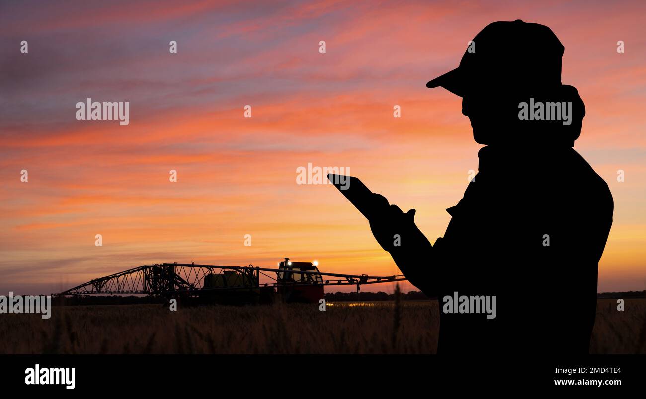 L'agricoltore controlla l'irroratrice con un tablet di notte. Agricoltura intelligente e agricoltura di precisione Foto Stock